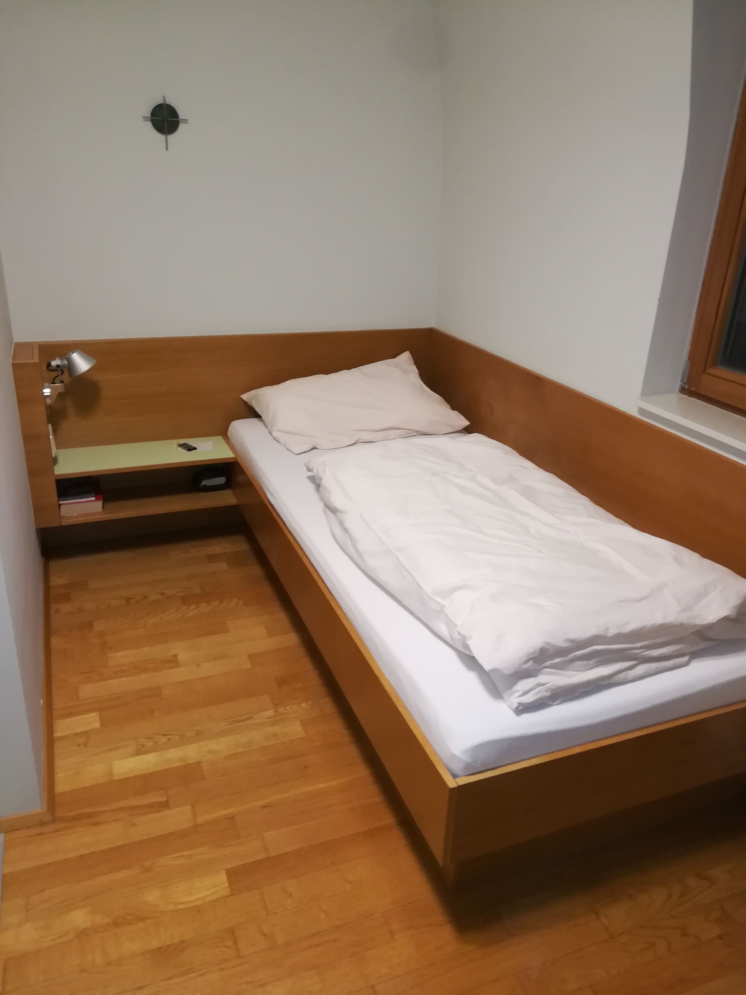 Jednolôžková izba s drevenou posteľou, nočným stolíkom a lampou.