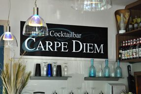 Pohľad do interiéru baru s nápisom "Cocktailbar Carpe Diem" na stene.