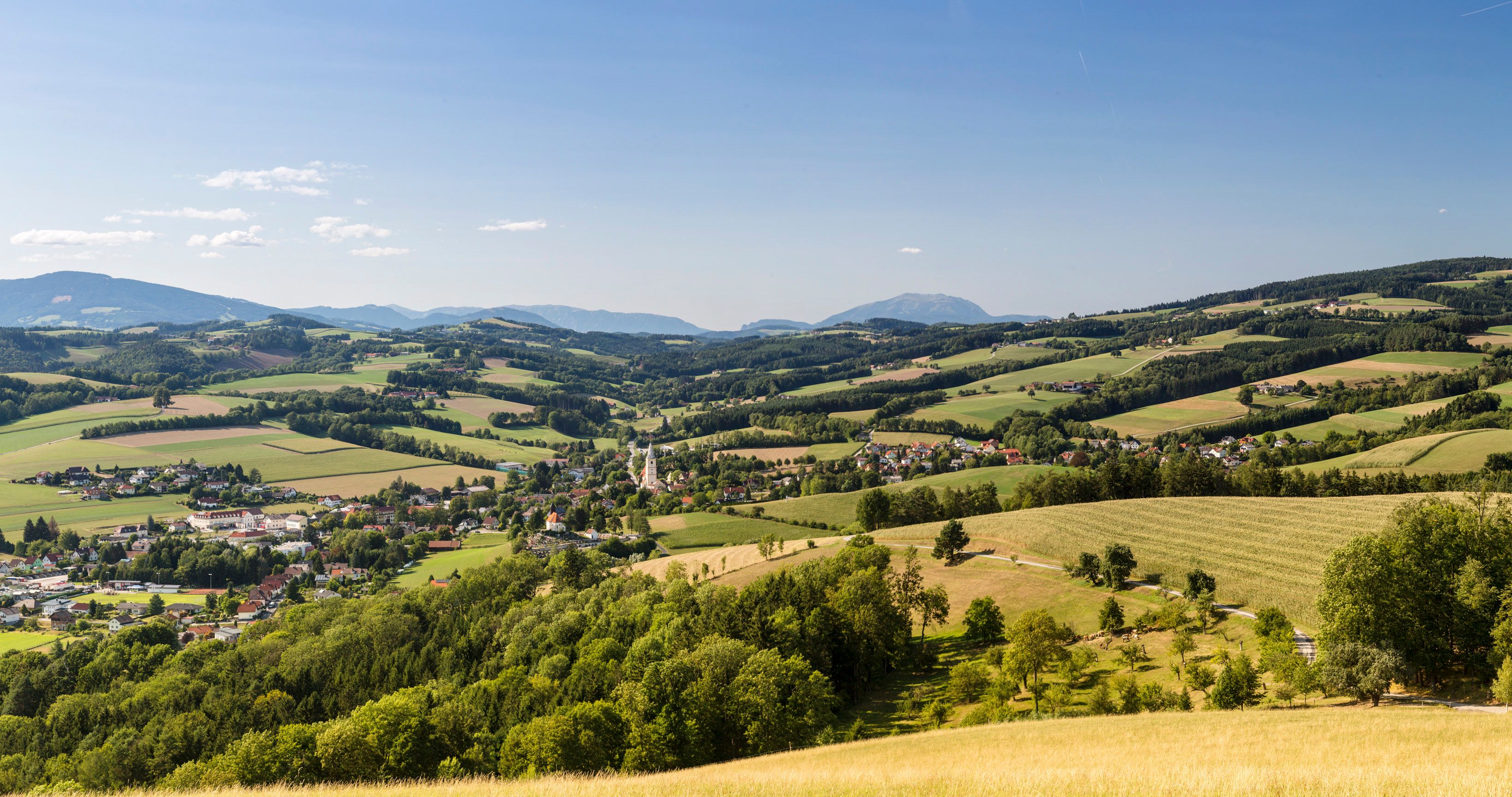 Panoramatický záber z oblasti Buckelige Welt, v údolí sa nachádza obec Krumbach s kostolnou vežou, v pozadí sú kopce a vrch Schneeberg.