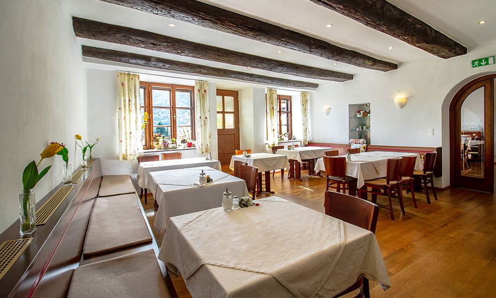 Útulná raňajková miestnosť s drevenými trámami, prestretými stolmi a kvetmi na parapetoch.