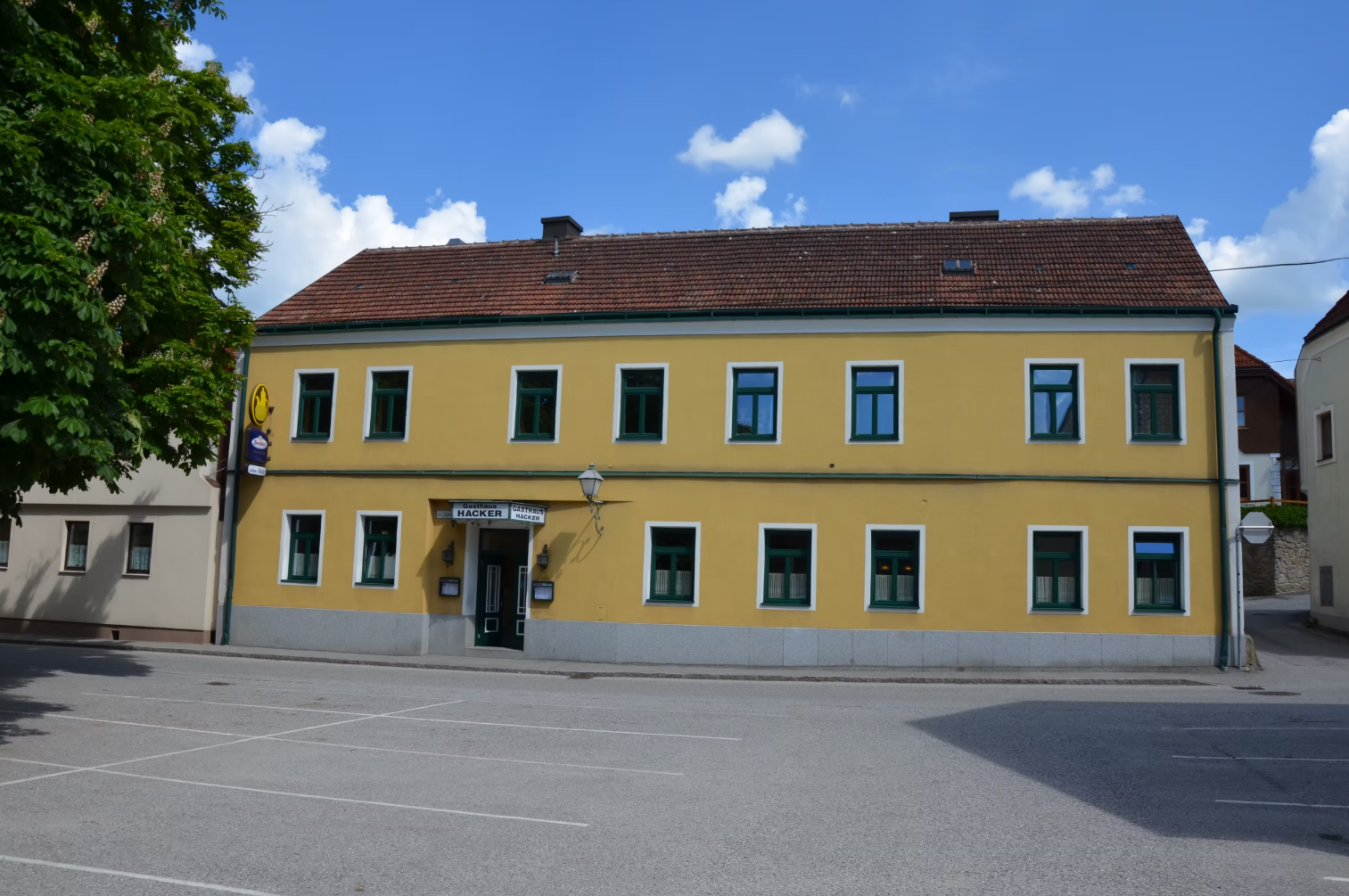 Žltá dvojpodlažná budova so zelenými okennými rámami a nápisom "Gasthaus Georg Hacker".
