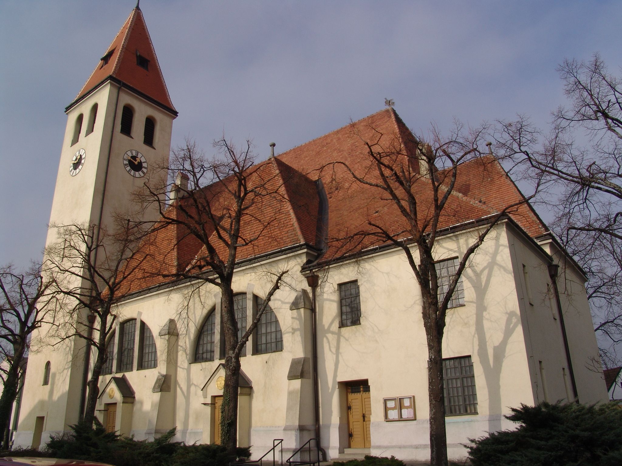 Kostol s vežou a červenou škridlovou strechou, obklopený holými stromami.