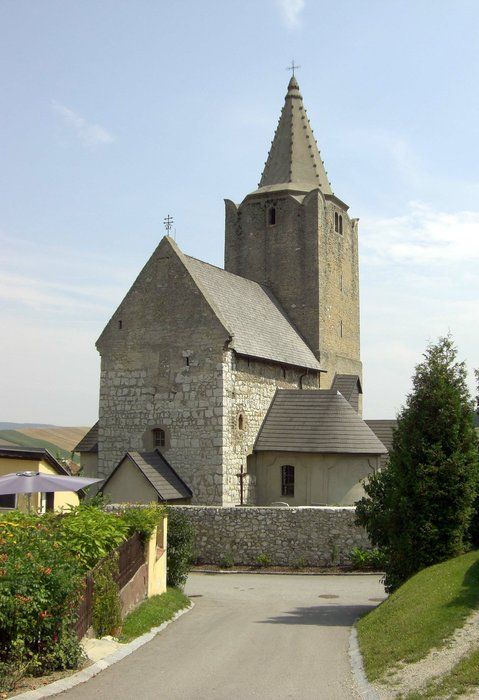 Historický opevnený kostol s kamennou vežou a špicatou strechou.