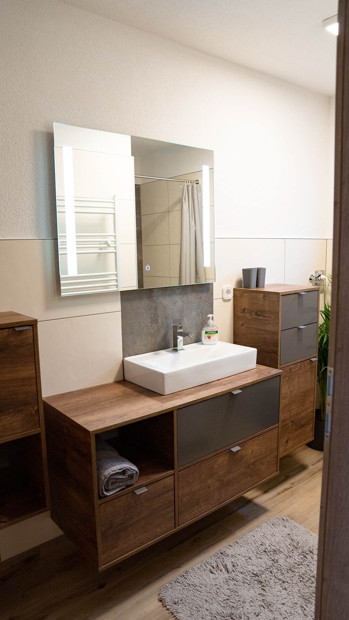 Moderná kúpeľňa s drevenými skrinkami, umývadlom a zrkadlom.