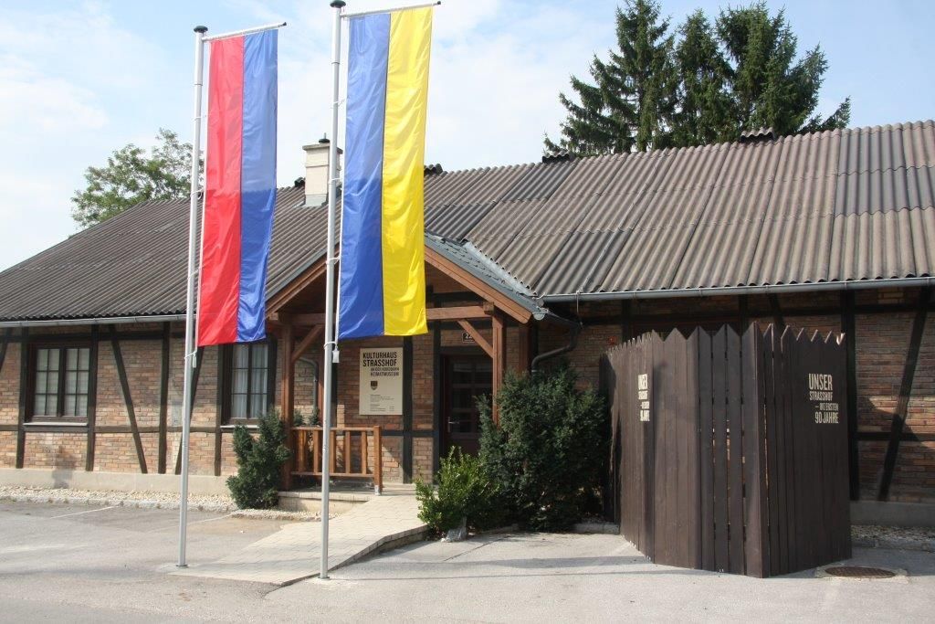 Vstup do múzea miestnej histórie Strasshof s dvoma stožiarmi a dreveným plotom.