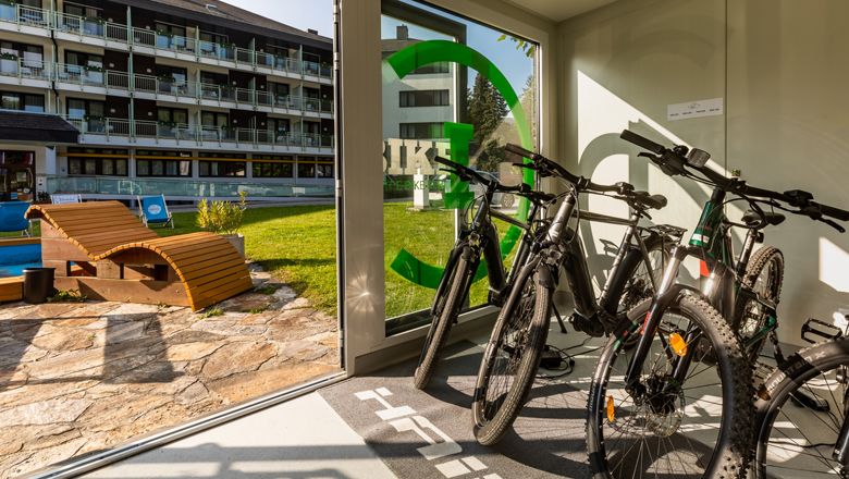 E-bicykle v požičovni s výhľadom do hotelovej záhrady.
