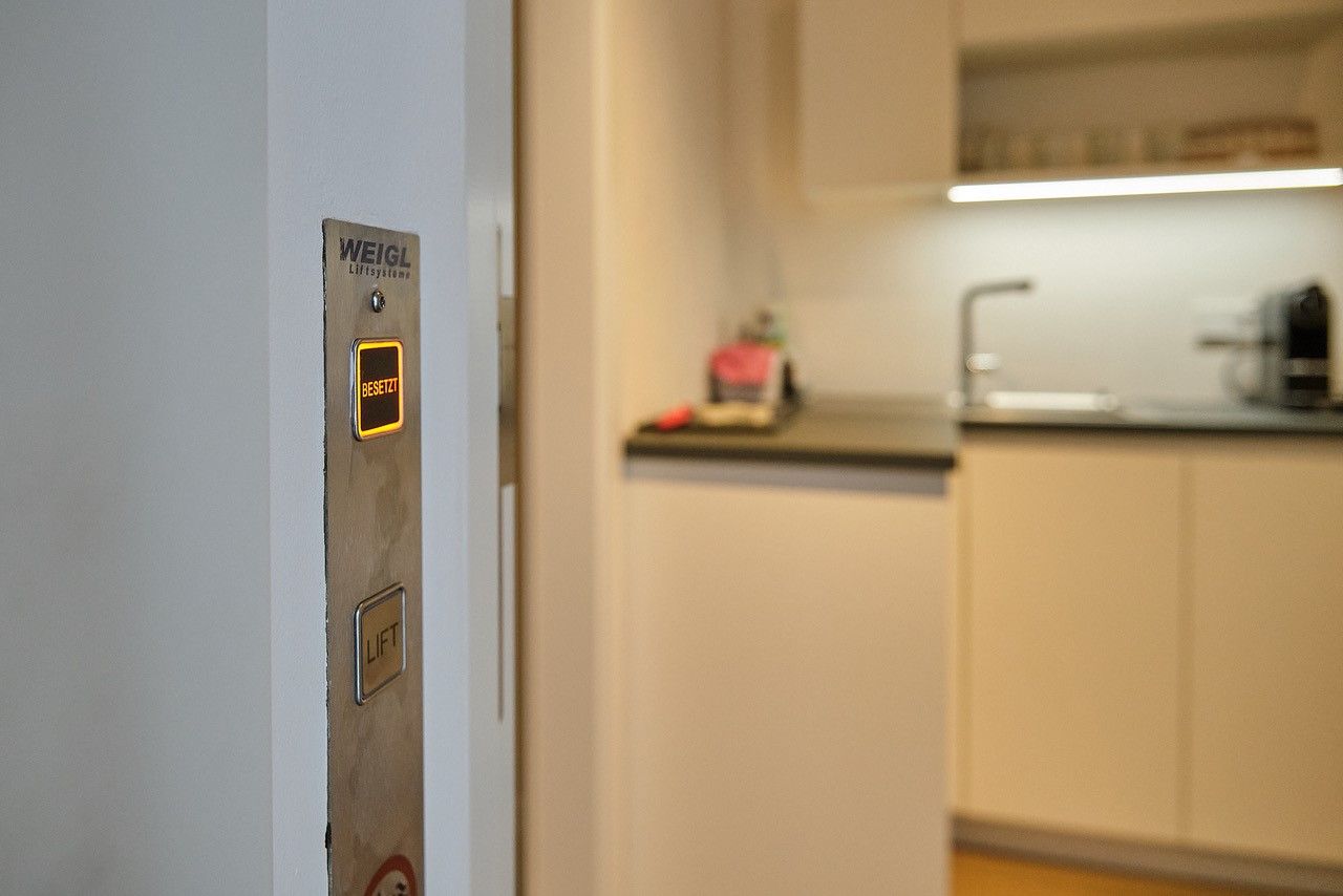 V modernej obývačke vedľa kuchyne sa rozsvieti tlačidlo výťahu s nápisom "Busy".