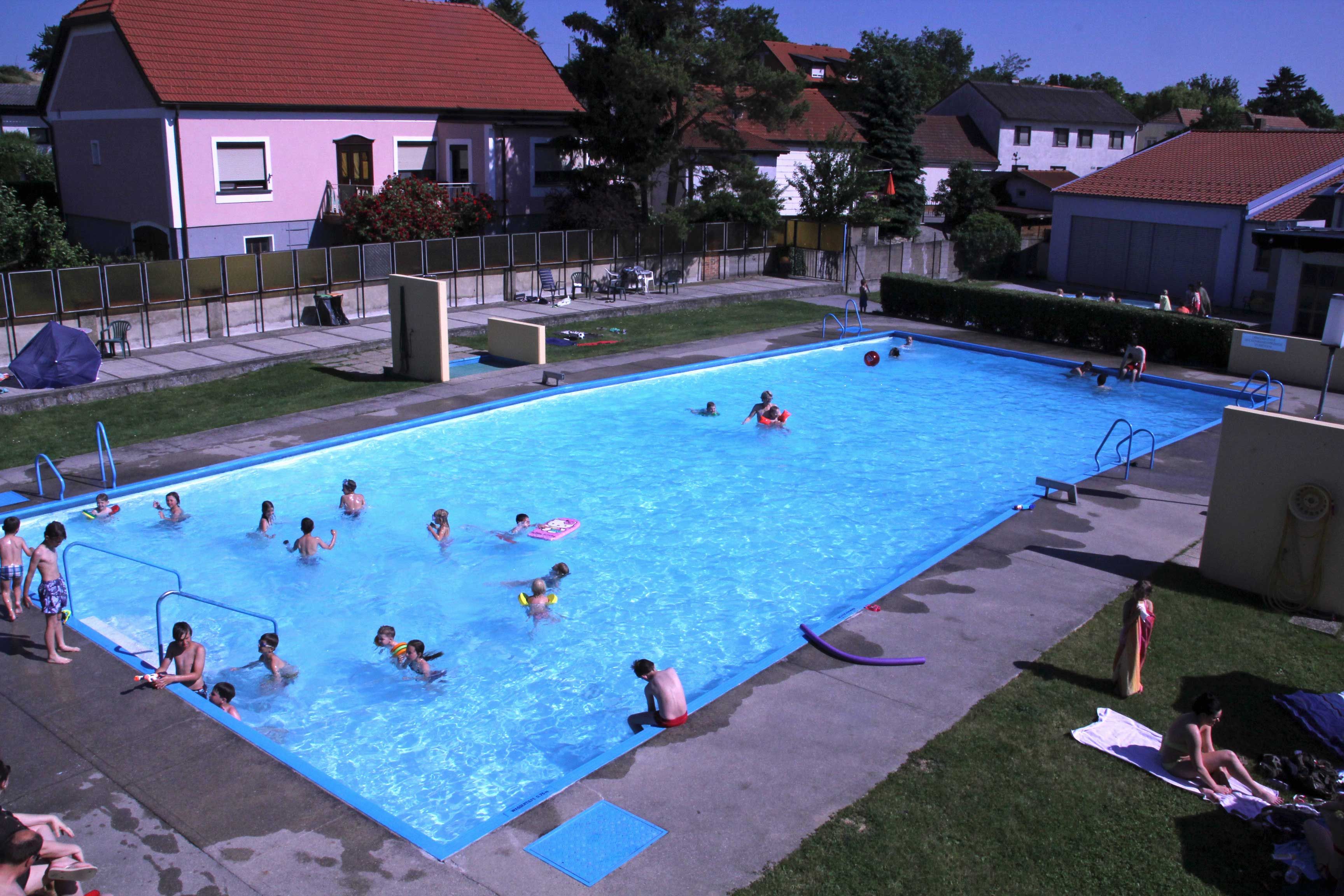 Vonkajší bazén s niekoľkými ľuďmi vo vode a na trávniku na opaľovanie.