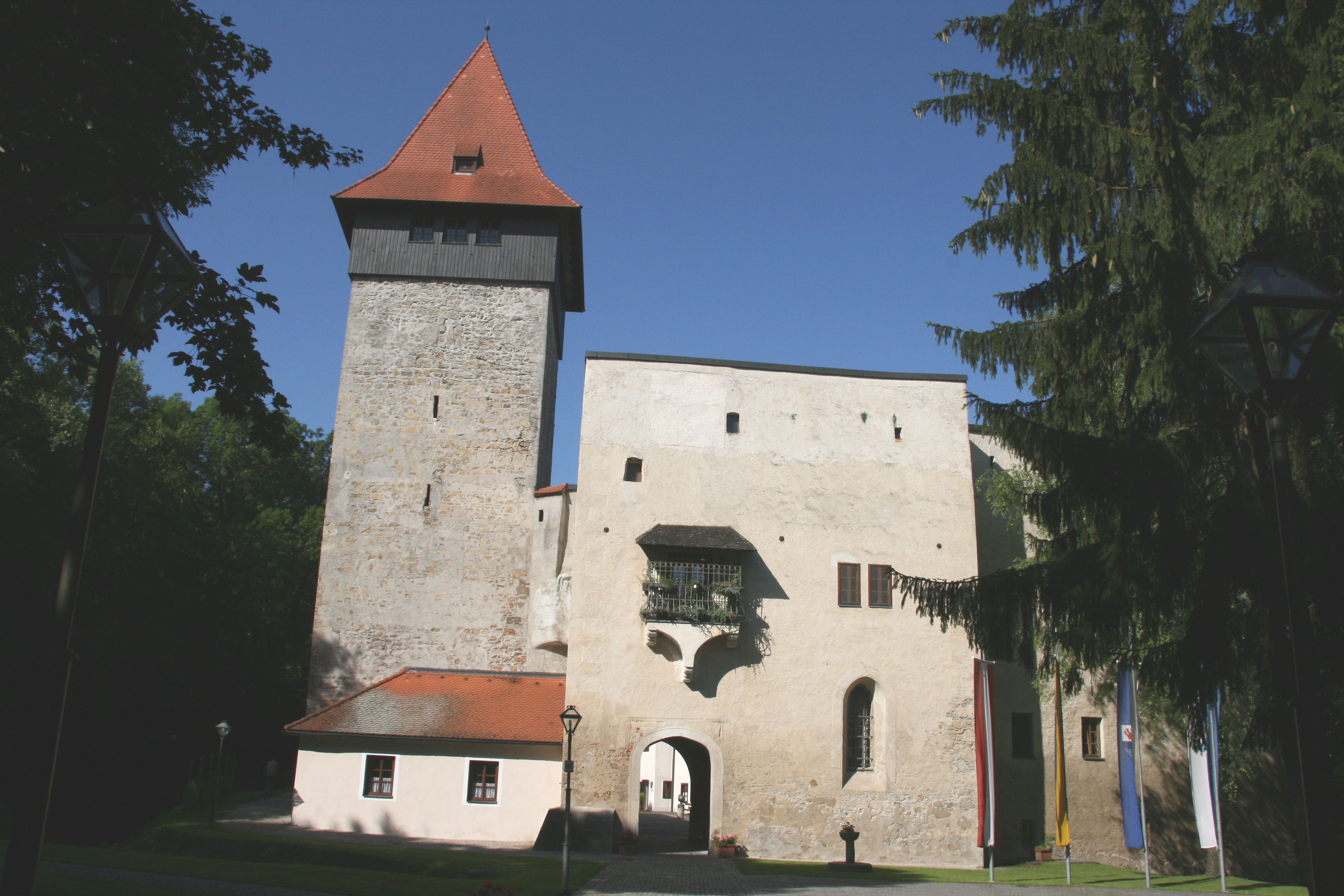 Hrad Ulmerfeld s vežou a vstupnou bránou, obklopený stromami a vlajkami.