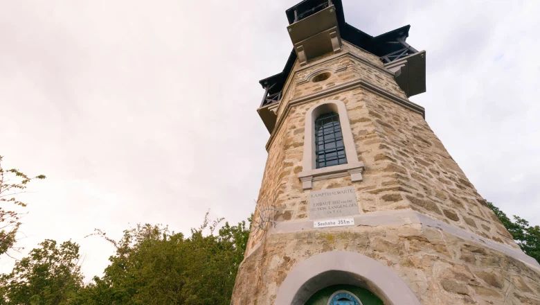 Kamenná rozhľadňa s oknami a nápisom, obklopená stromami.