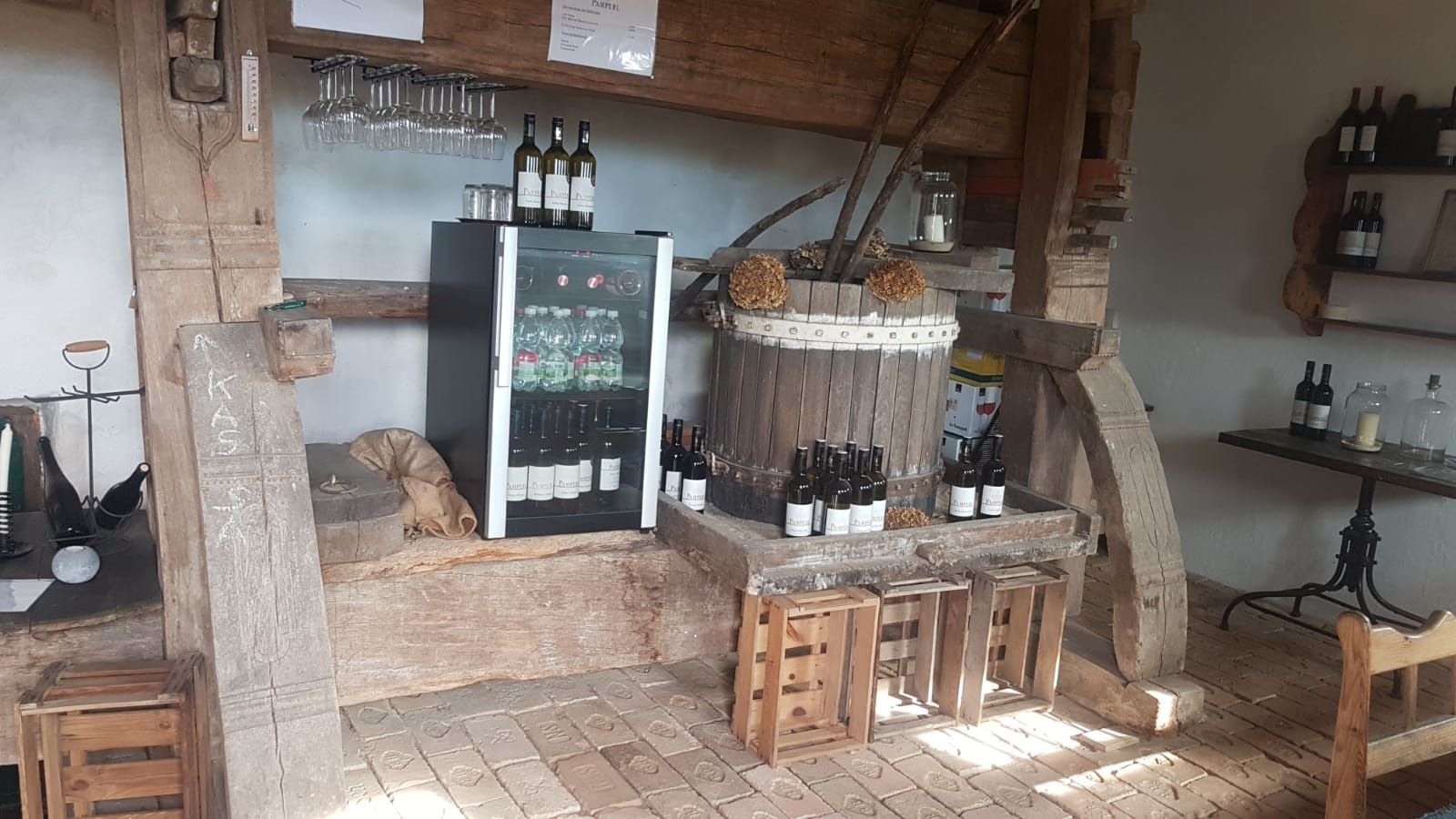 Pohľad do interiéru rustikálnej vinárne s fľašami vína, pohármi a chladničkou.