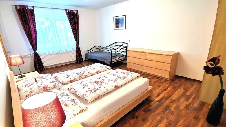 Spálňa s manželskou posteľou, samostatnou posteľou, komodou a kvetmi vo váze.