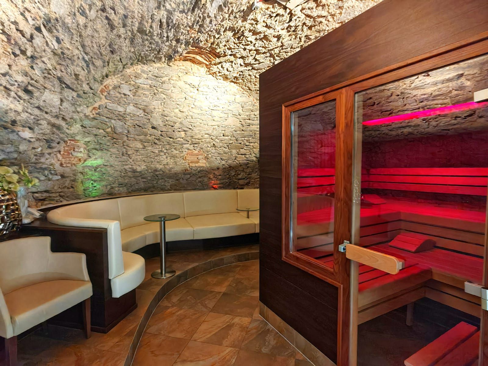 Útulný wellness priestor so saunou a posedením v miestnosti s klenutou kamennou stenou.