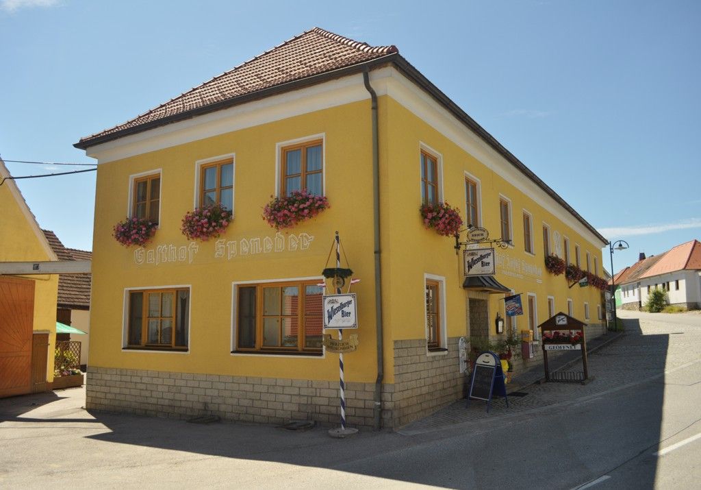 Žltá budova s nápisom "Gasthof Speneder", zdobená kvetmi.