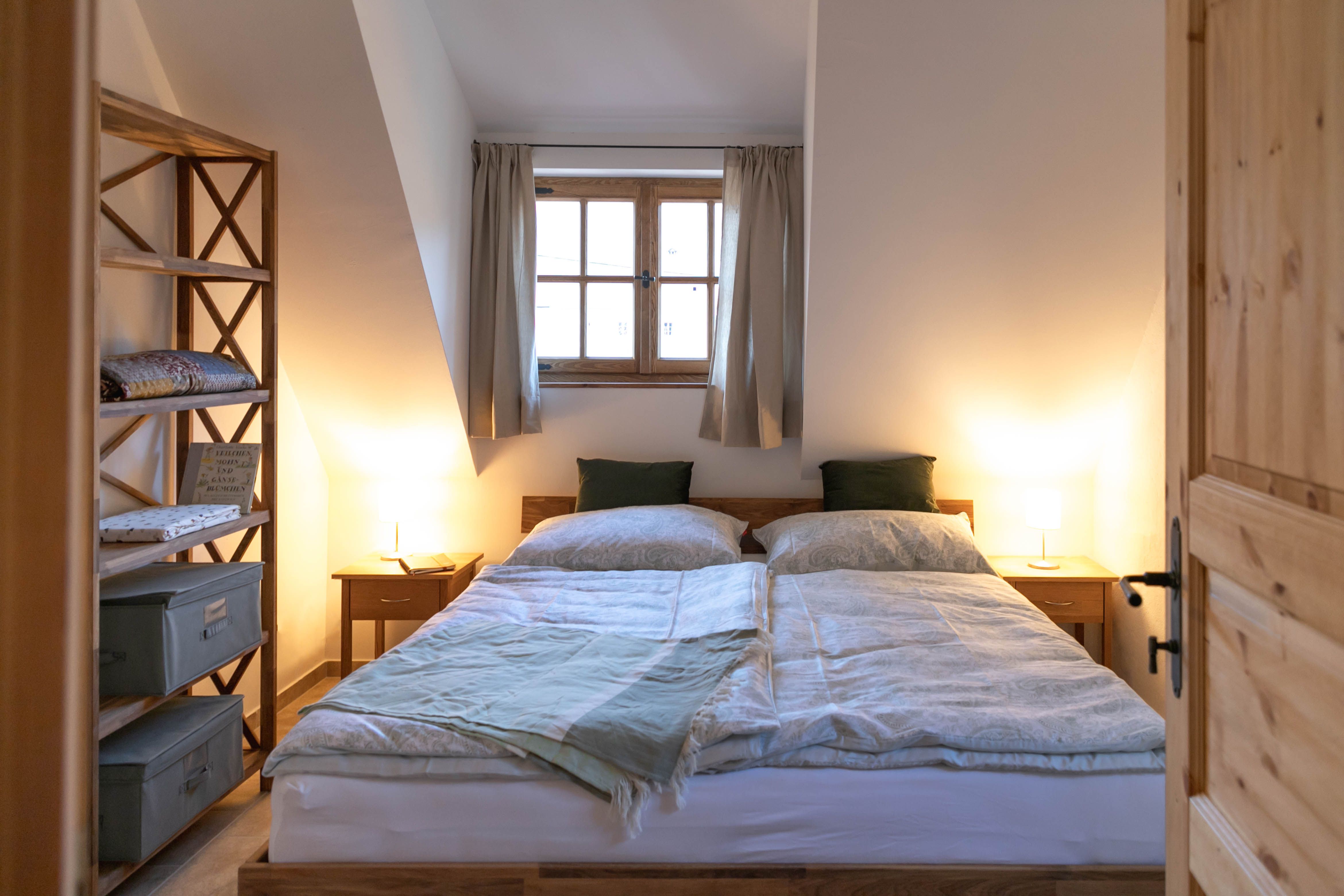 Útulná spálňa s manželskou posteľou, dreveným nábytkom a oknom so závesmi.