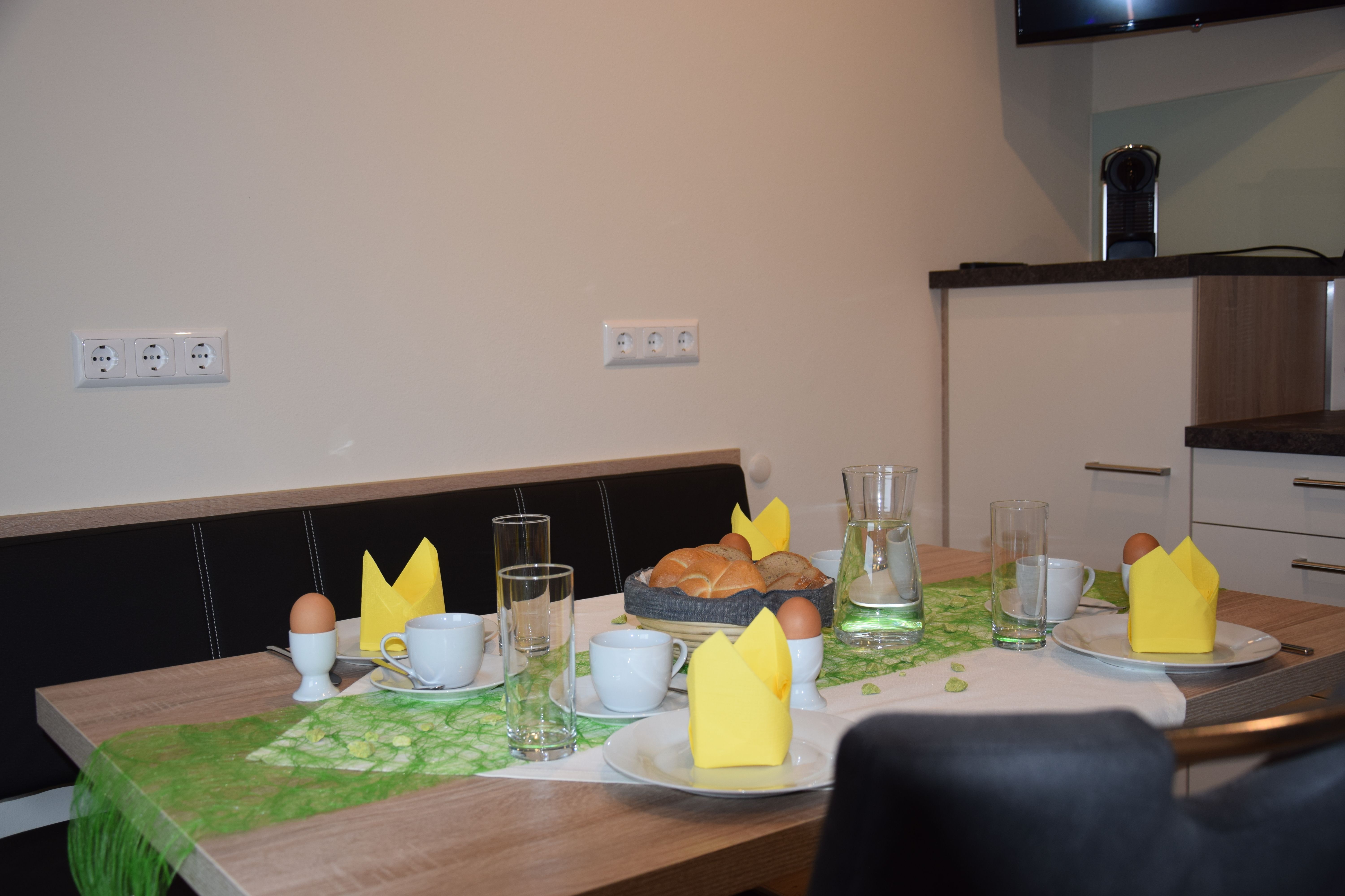 Raňajkový stôl s chlebíčkami, vajíčkami, šálkami a žltými obrúskami.