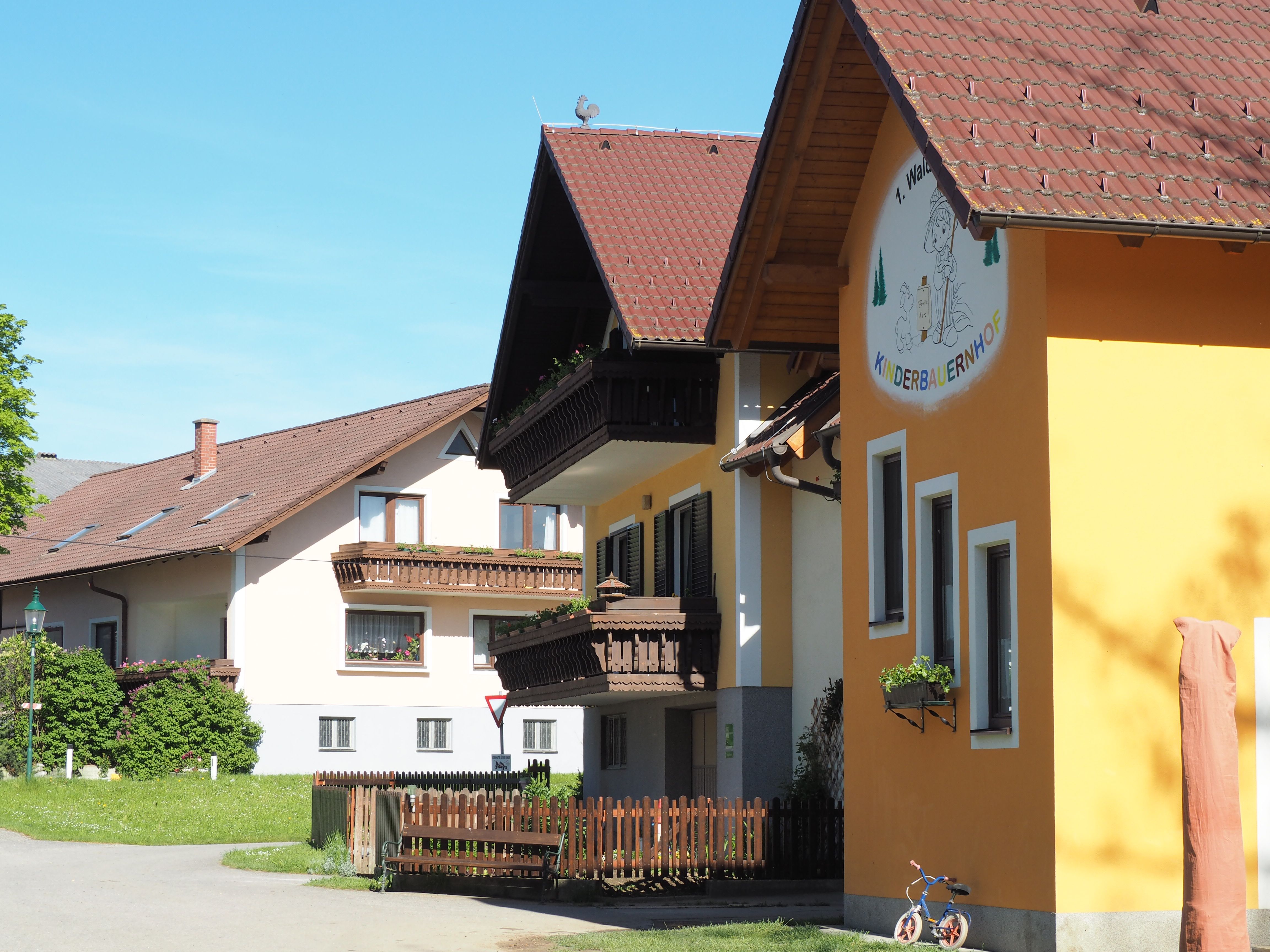 Budova detskej farmy Waldviertel so žltou fasádou a drevenými balkónmi, obklopená zelenou krajinou.