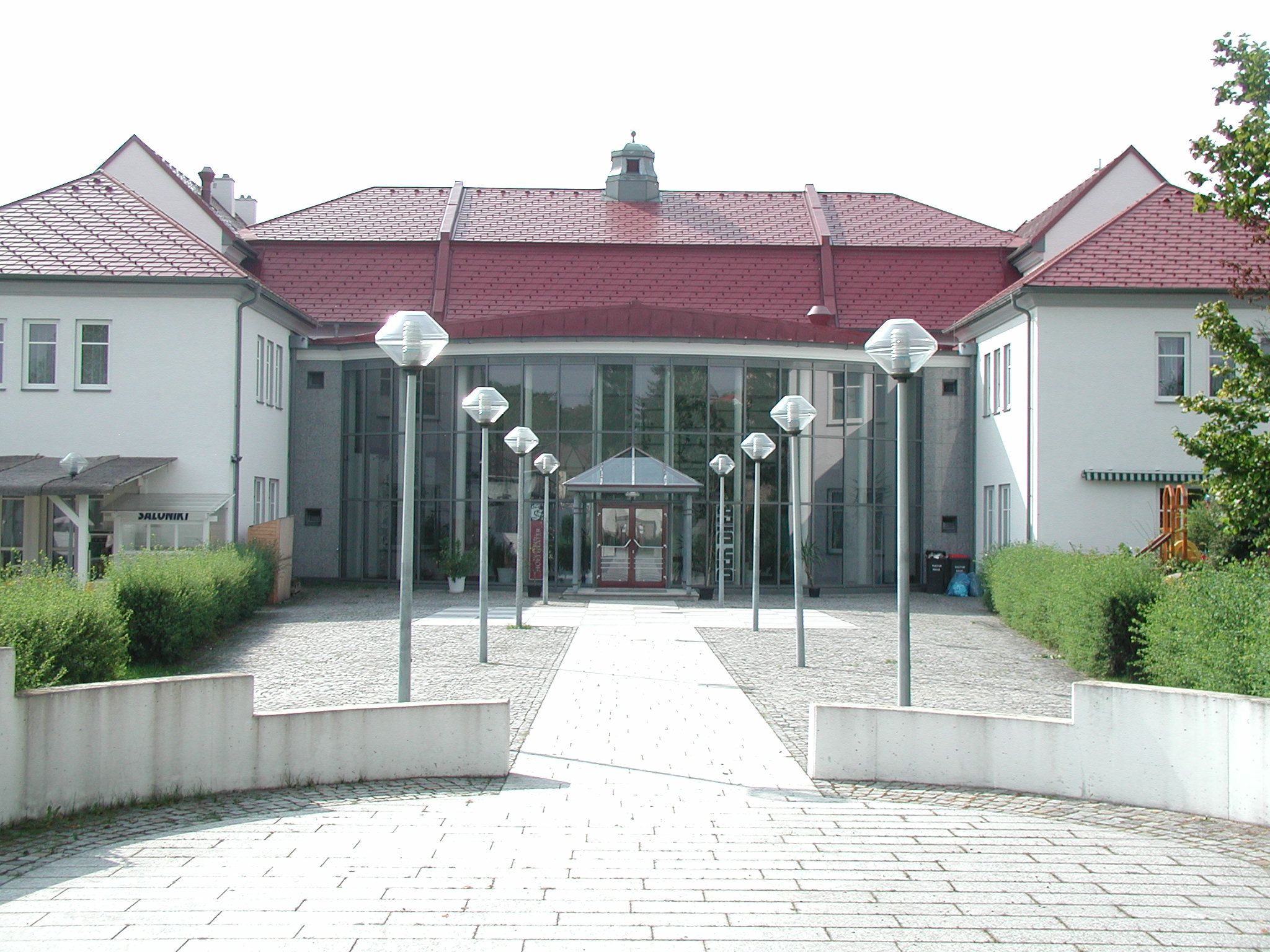 Vchod do moderného kultúrneho centra so sklenenou fasádou a červenými strechami.