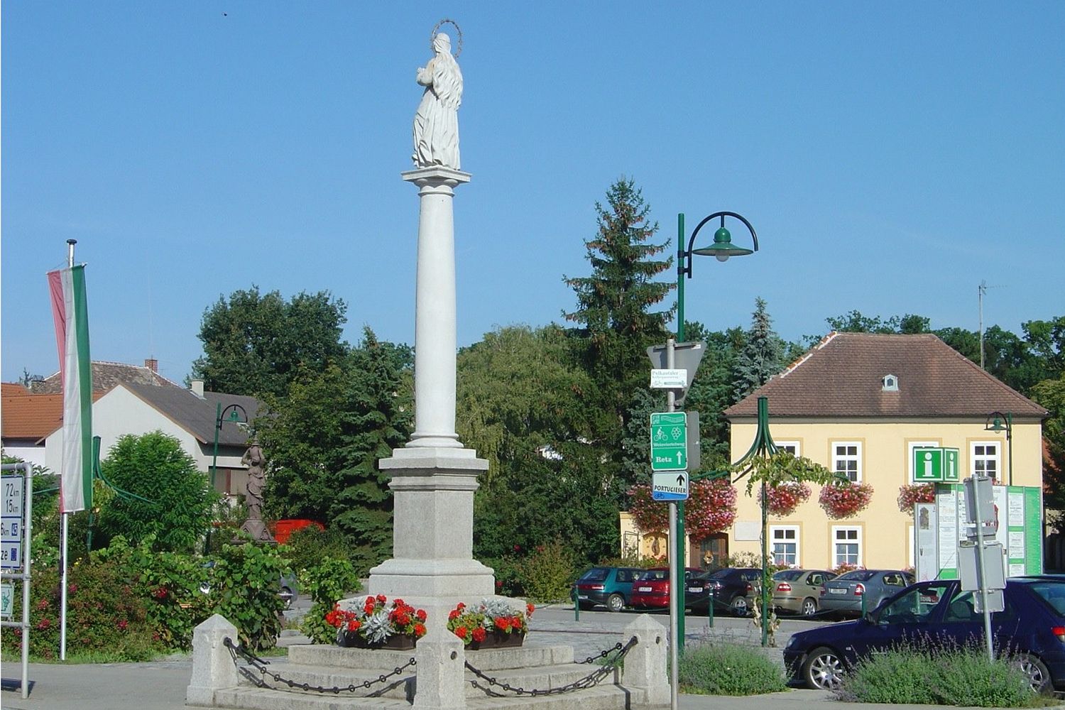 Socha na stĺpe na námestí v Haugsdorfe, obklopená budovami a stromami.
