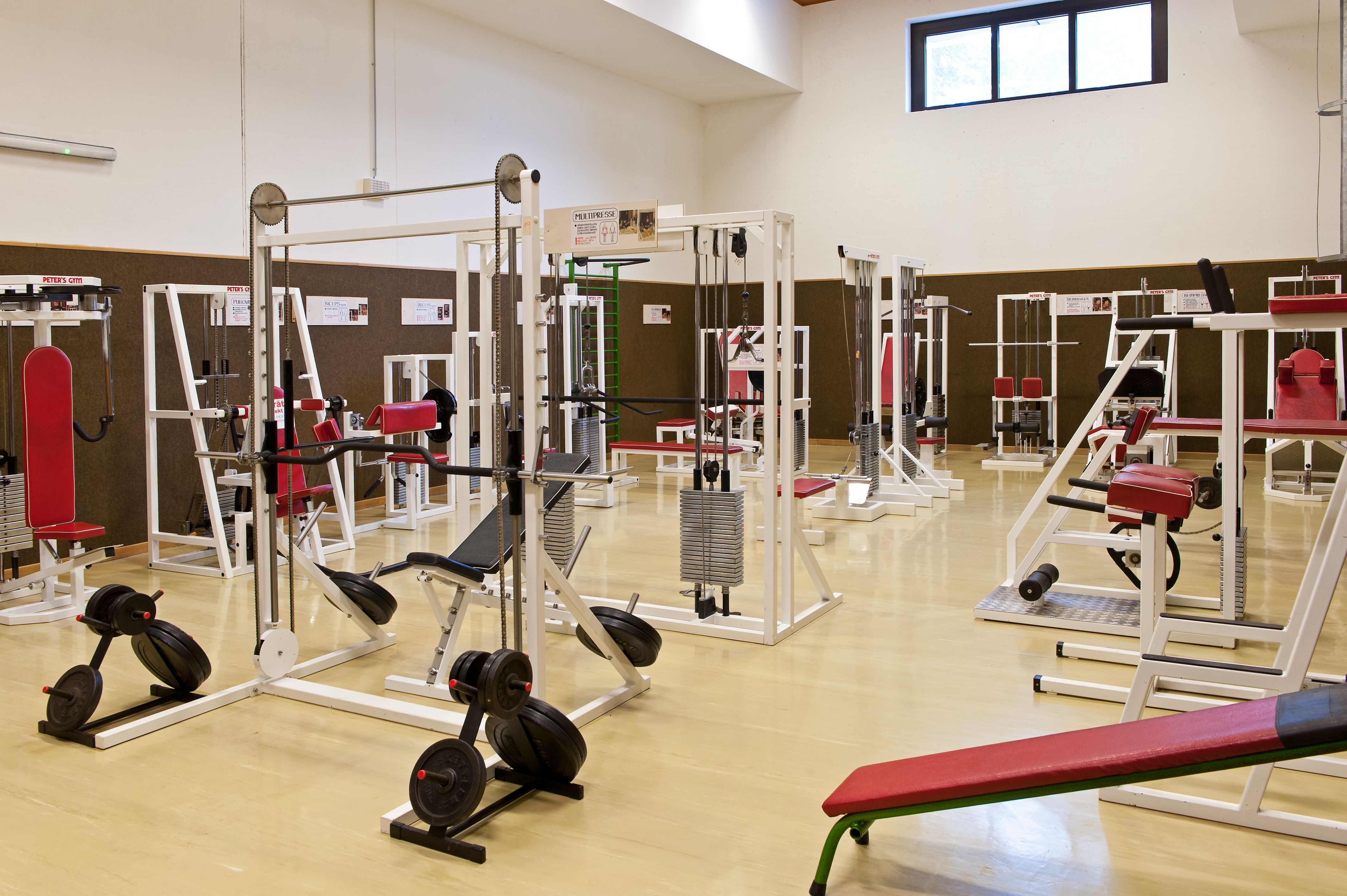 Fitness štúdio s rôznymi cvičebnými strojmi a červenými vankúšmi.