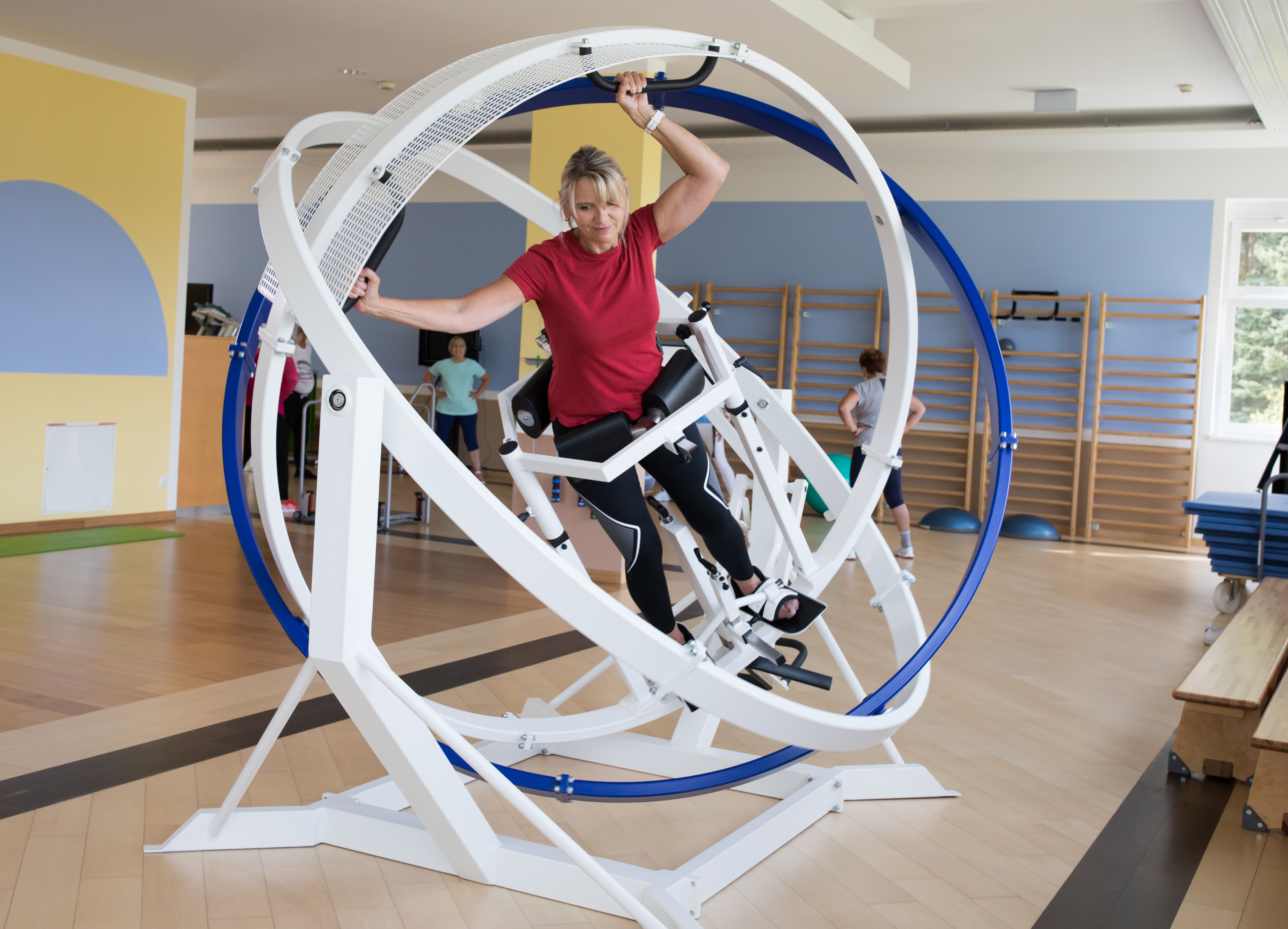 Žena cvičí na posilňovacom stroji s rotujúcimi kruhmi vo fitnescentre.