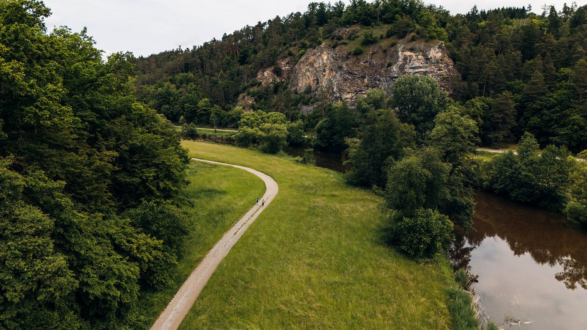 Dvaja ľudia kráčajú pozdĺž rieky Thaya obklopení mohutnými skalami a stromami
