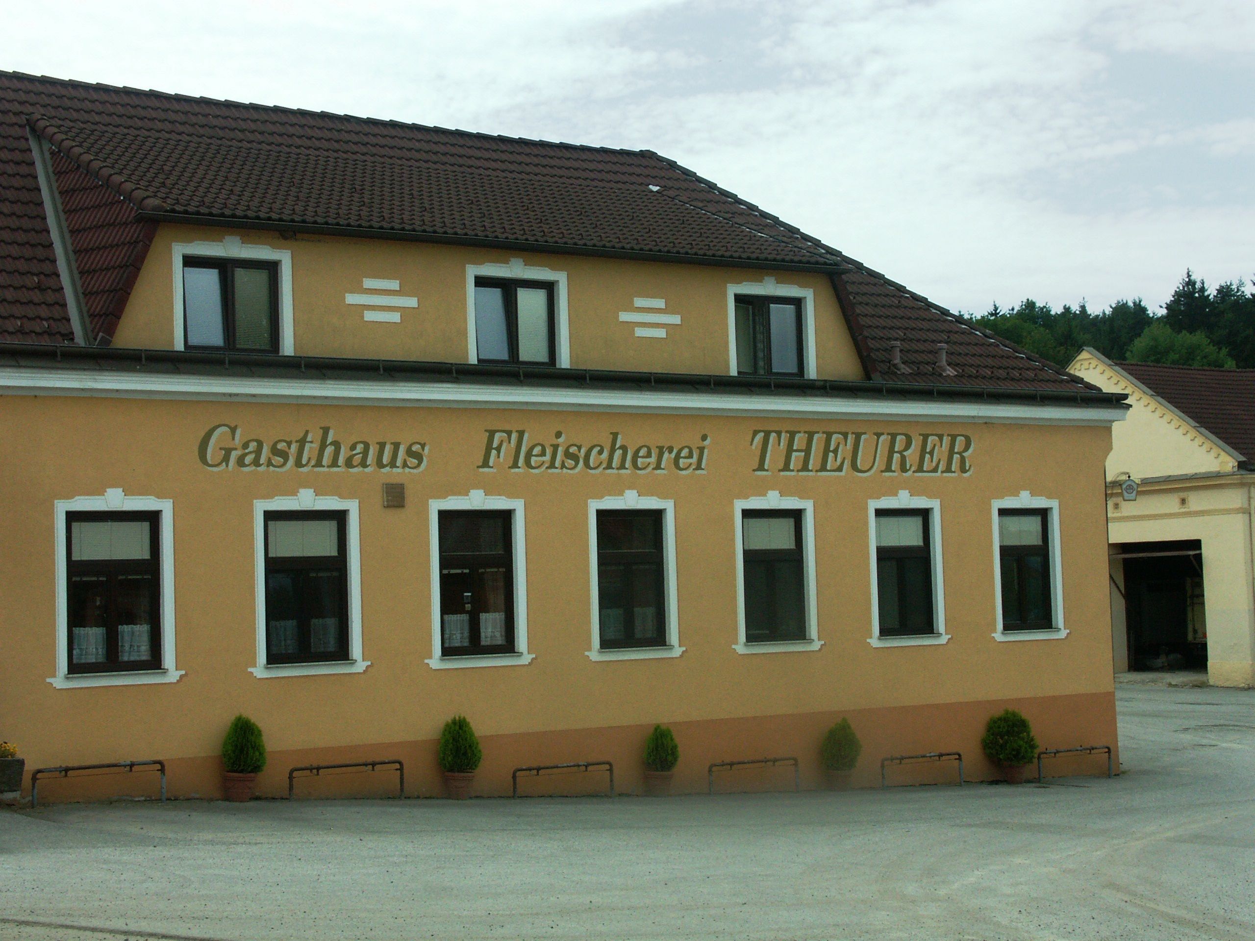Exteriérový pohľad na hostinec a mäsiarstvo Theurer so žltou fasádou a hnedou strechou.