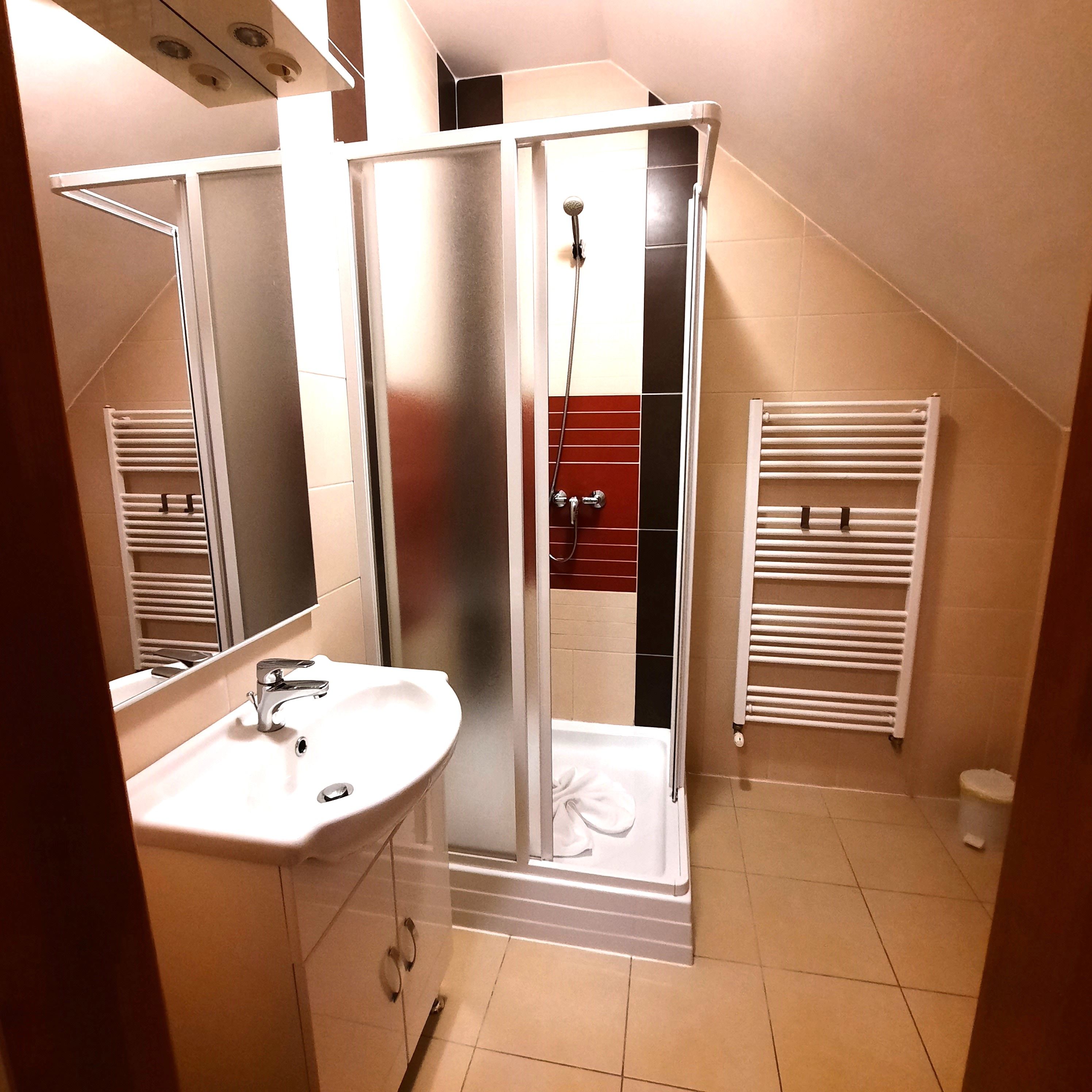 Moderná kúpeľňa so sprchovacím kútom, umývadlom a radiátorom na uteráky.