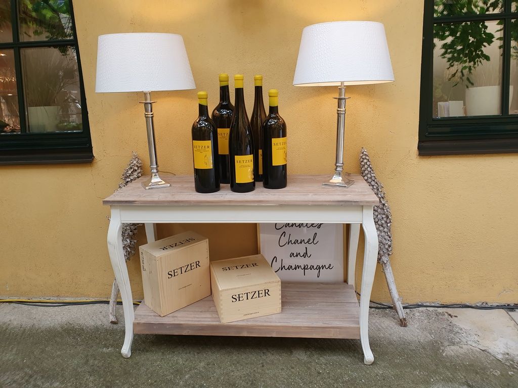 Konzolový stolík s fľašami na víno, lampami a drevenými debničkami.