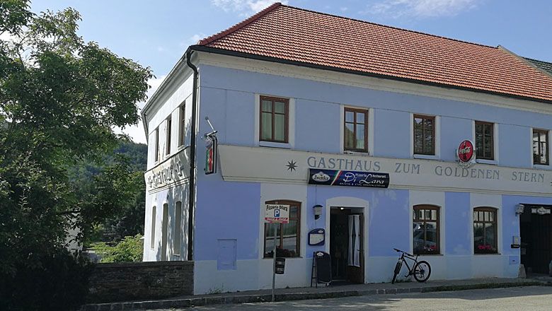 Dvojposchodová budova s nápisom "Gasthaus zum Goldenen Stern" a bicyklom pred ňou.