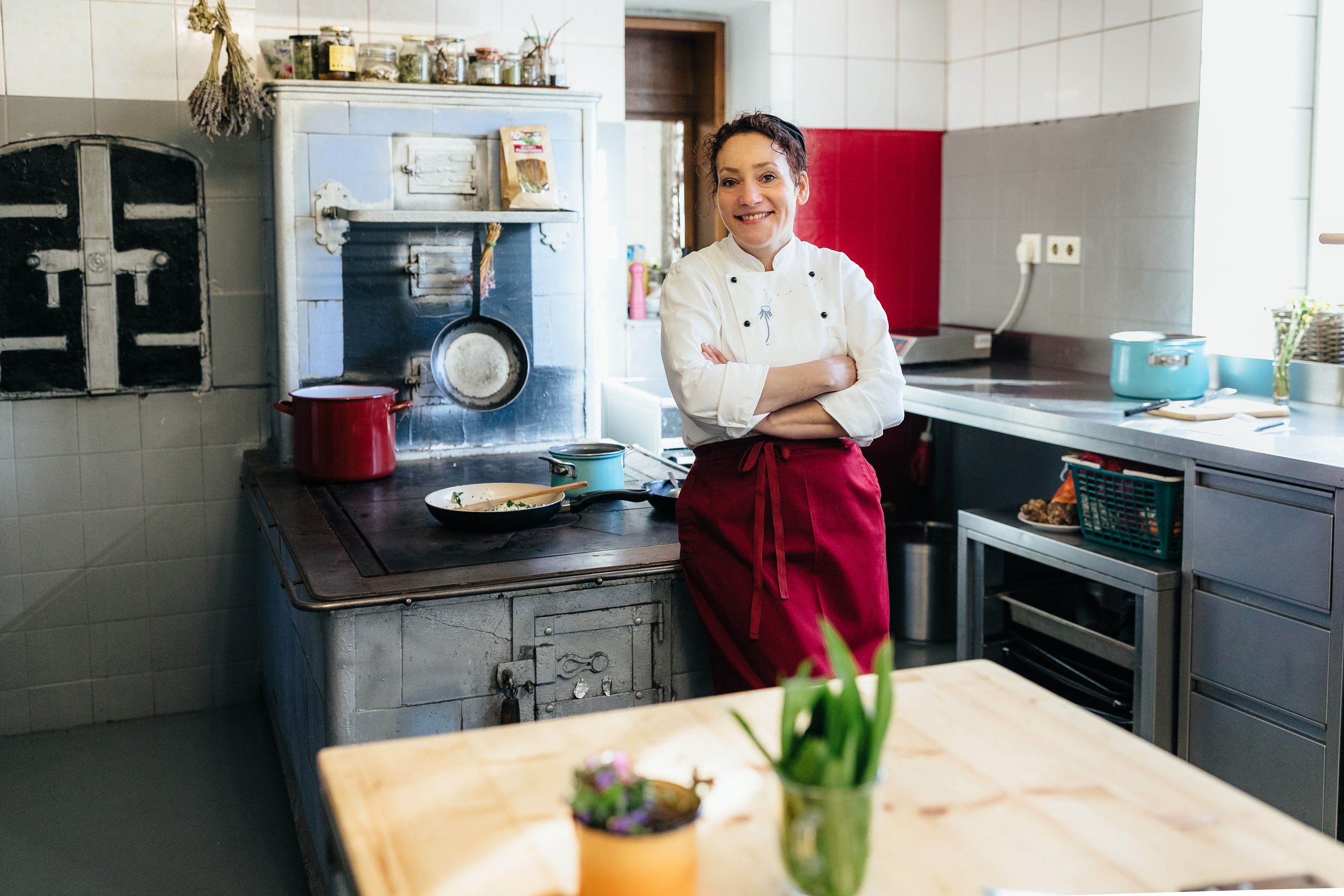 Kuchár v bielom saku a červenej zástere stojí v kuchyni pred starým sporákom.