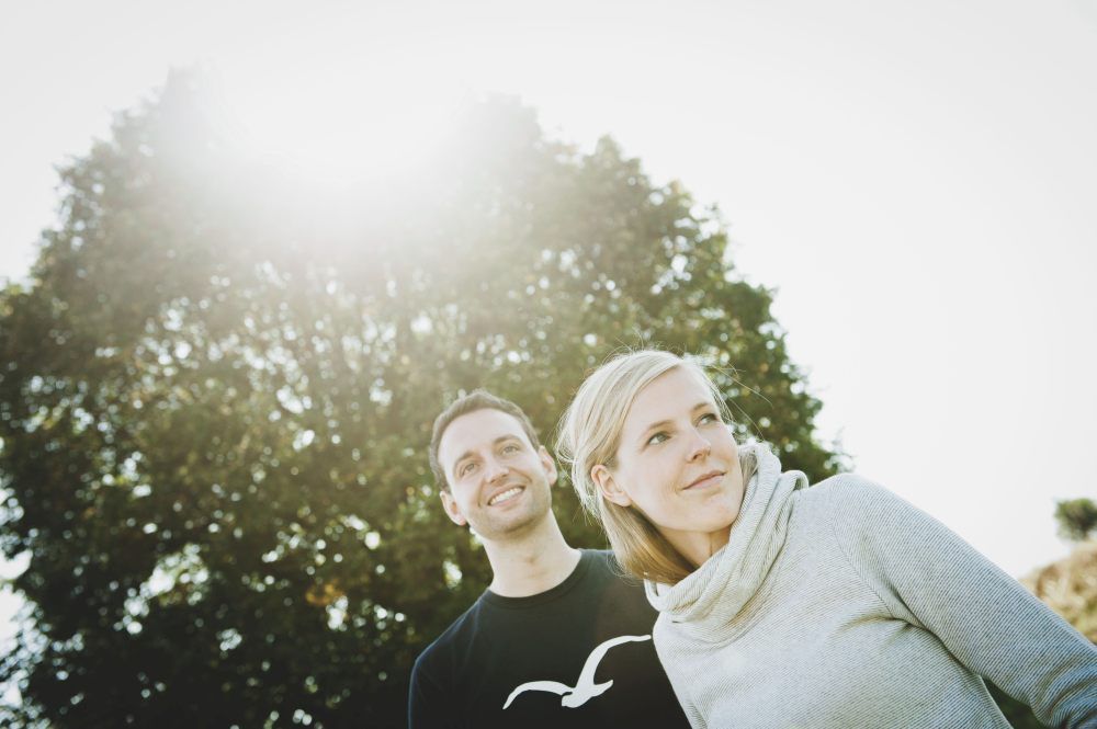 Muž a žena stoja vonku pred stromom a cez listy presvitá slnko.