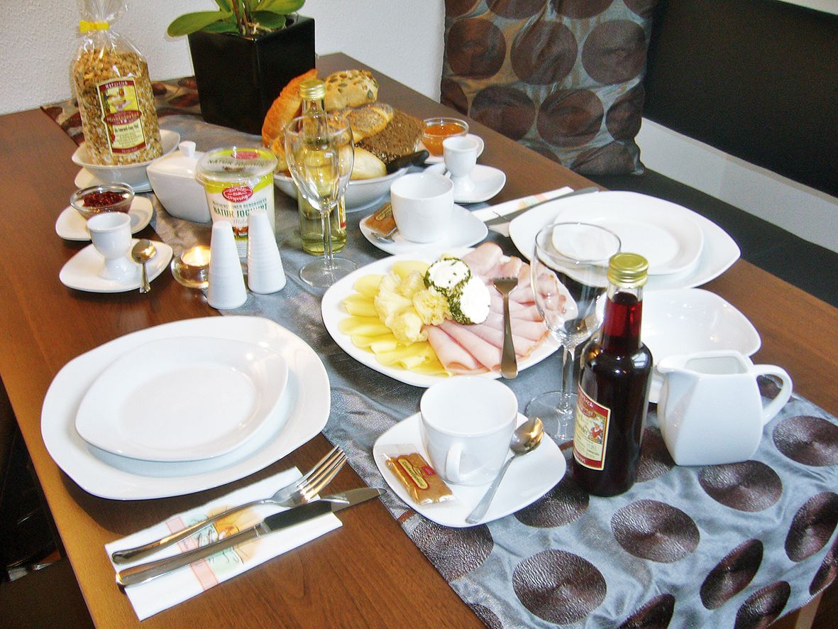 Raňajkový stôl s riadom, údeninami, chlebom, müsli a nápojmi.