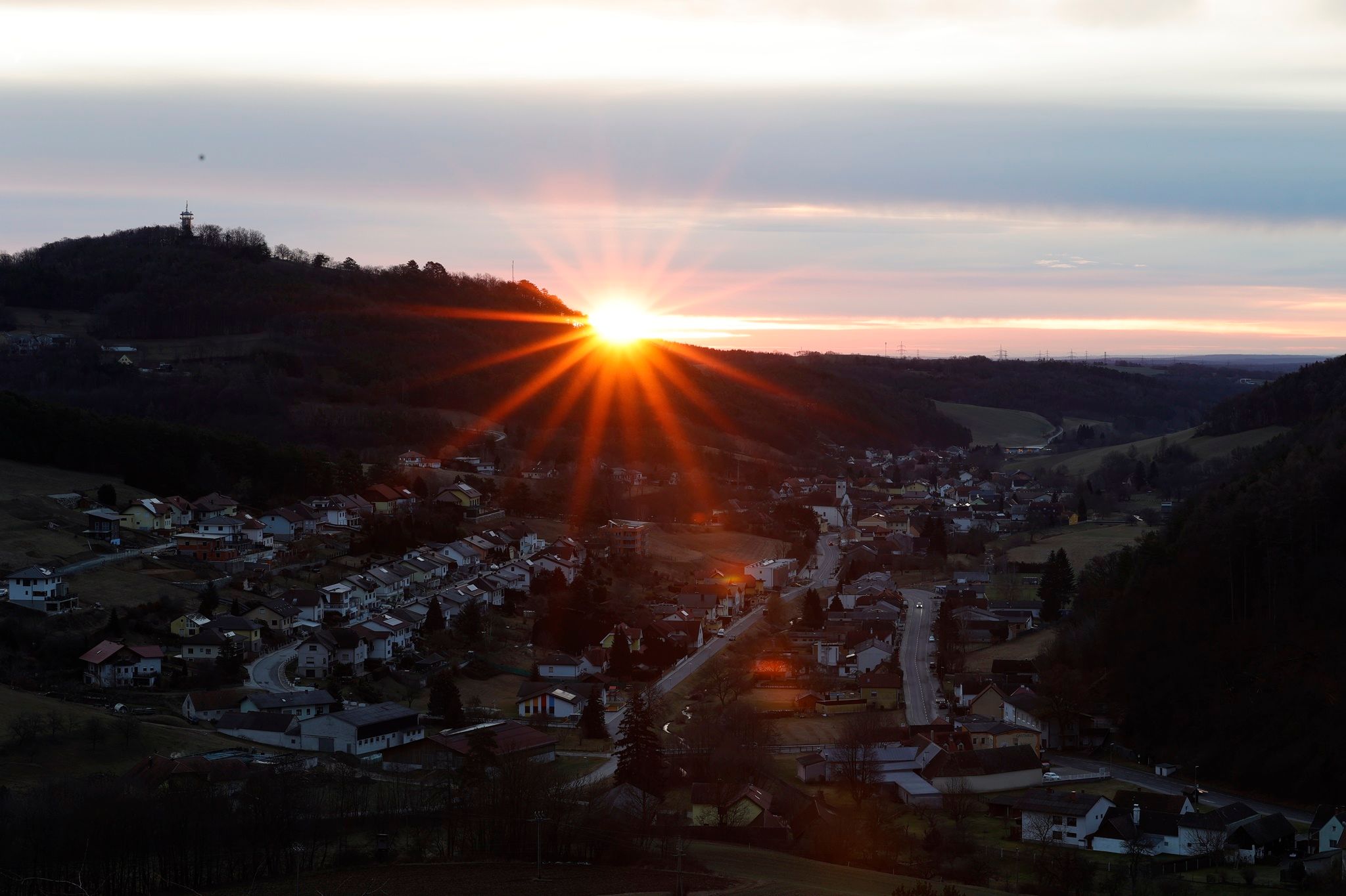 Východ slnka za kopcom s dedinou v popredí.