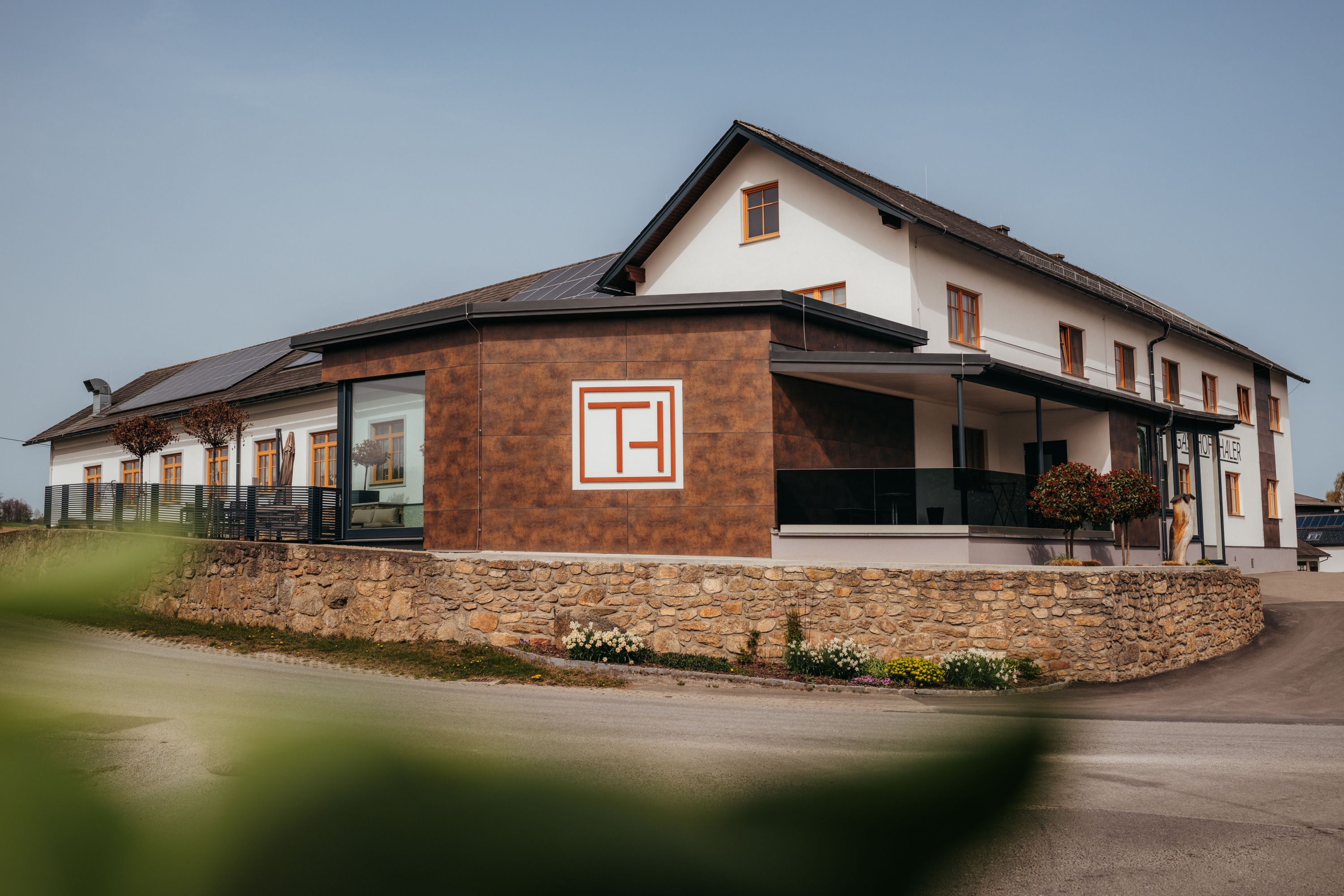 Moderná budova s označením "Gasthof Thaler", obklopená kamenným múrom a rastlinami.