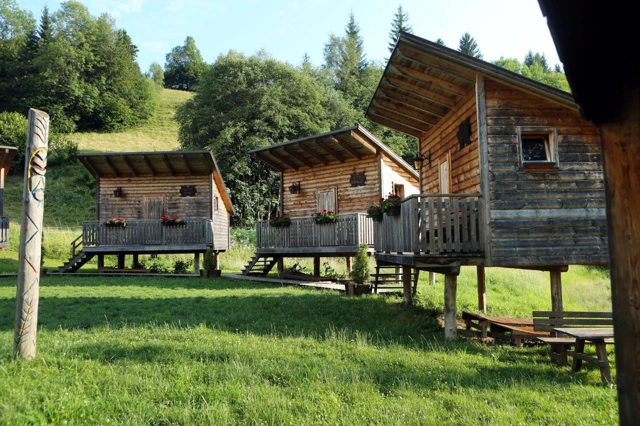 Tri drevené chatky na koloch s verandami v zelenej zalesnenej oblasti.