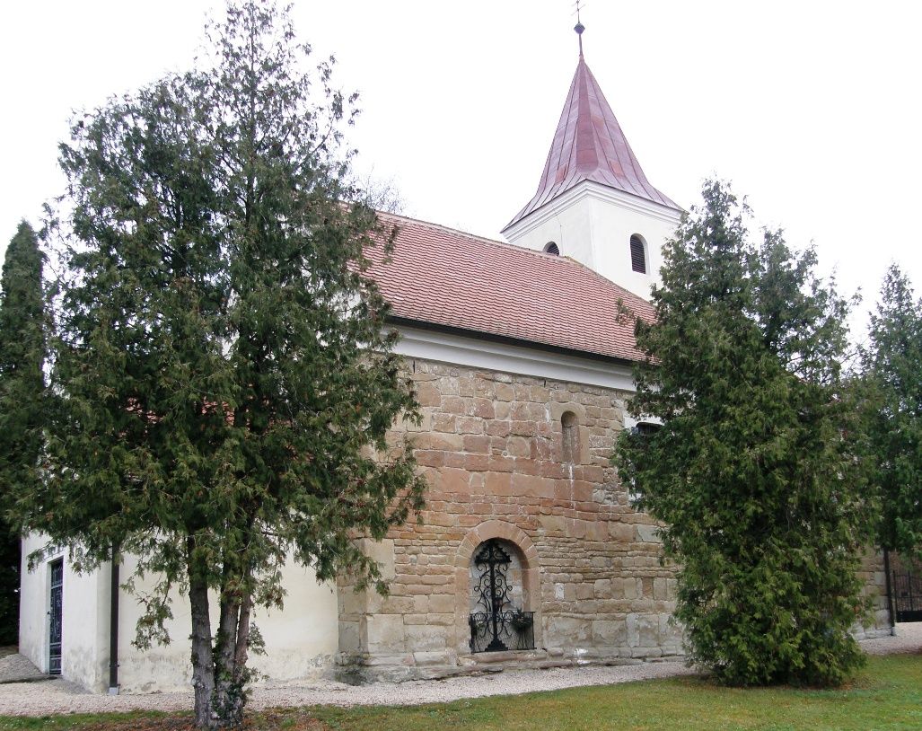 Starý kostol s červenou škridlovou strechou a vežou, obklopený stromami.