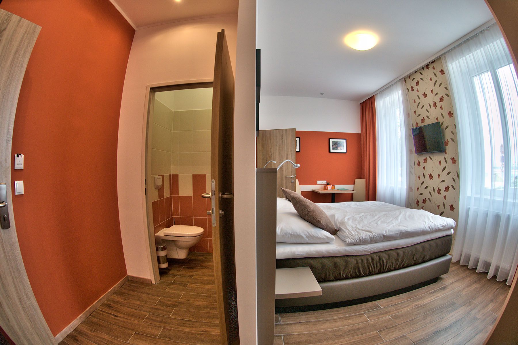 Moderná izba pre hostí s manželskou posteľou, písacím stolom a televízorom. Vedľa nej je malá kúpeľňa s WC.