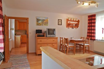 Útulná obývacia izba s dreveným nábytkom, jedálenským stolom, TV a červenými závesmi.