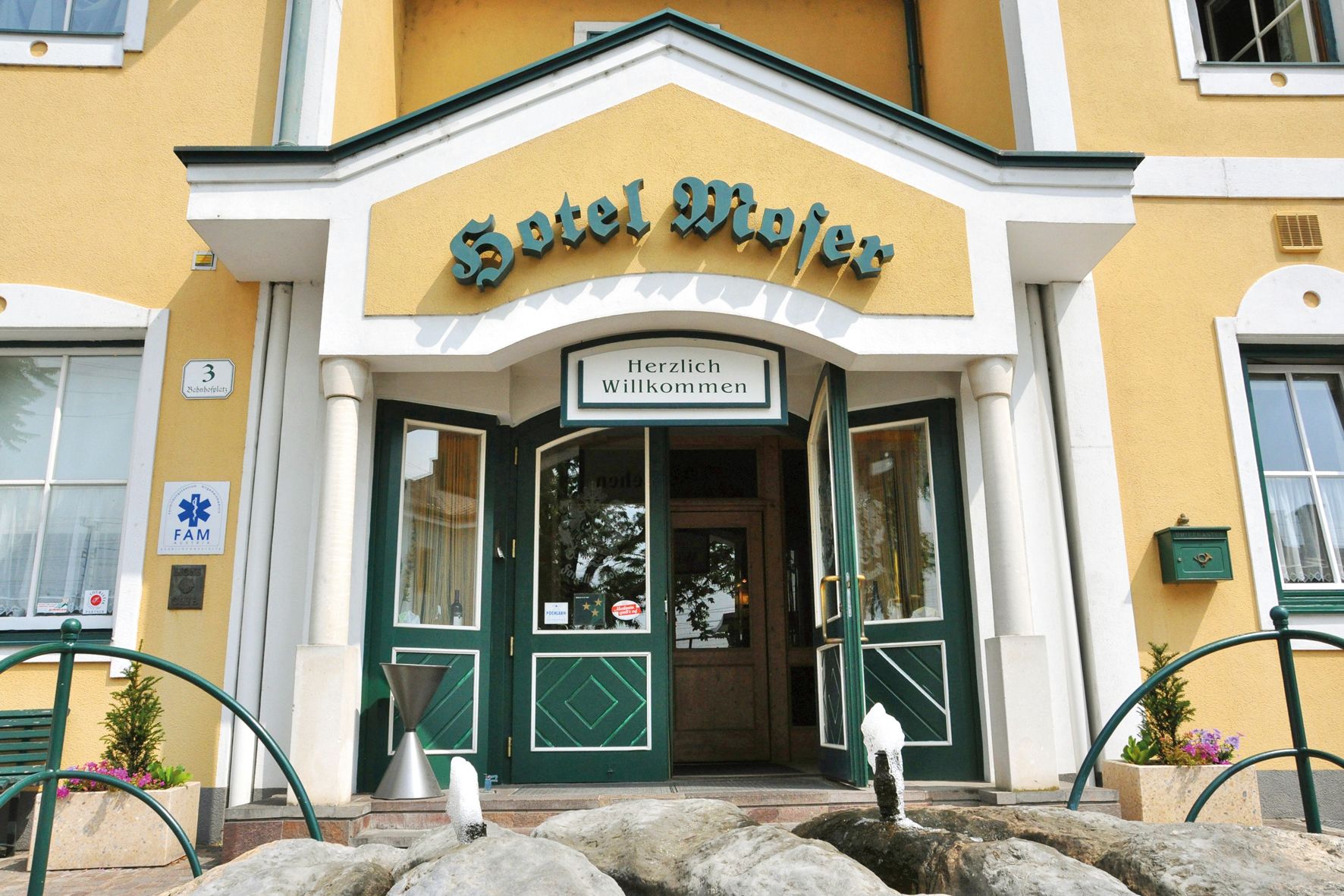 Vchod do hotela Moser so žltou fasádou a zelenými dverami.