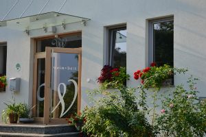 Vchod do budovy s nápisom "wein + bett", obklopený kvetmi.