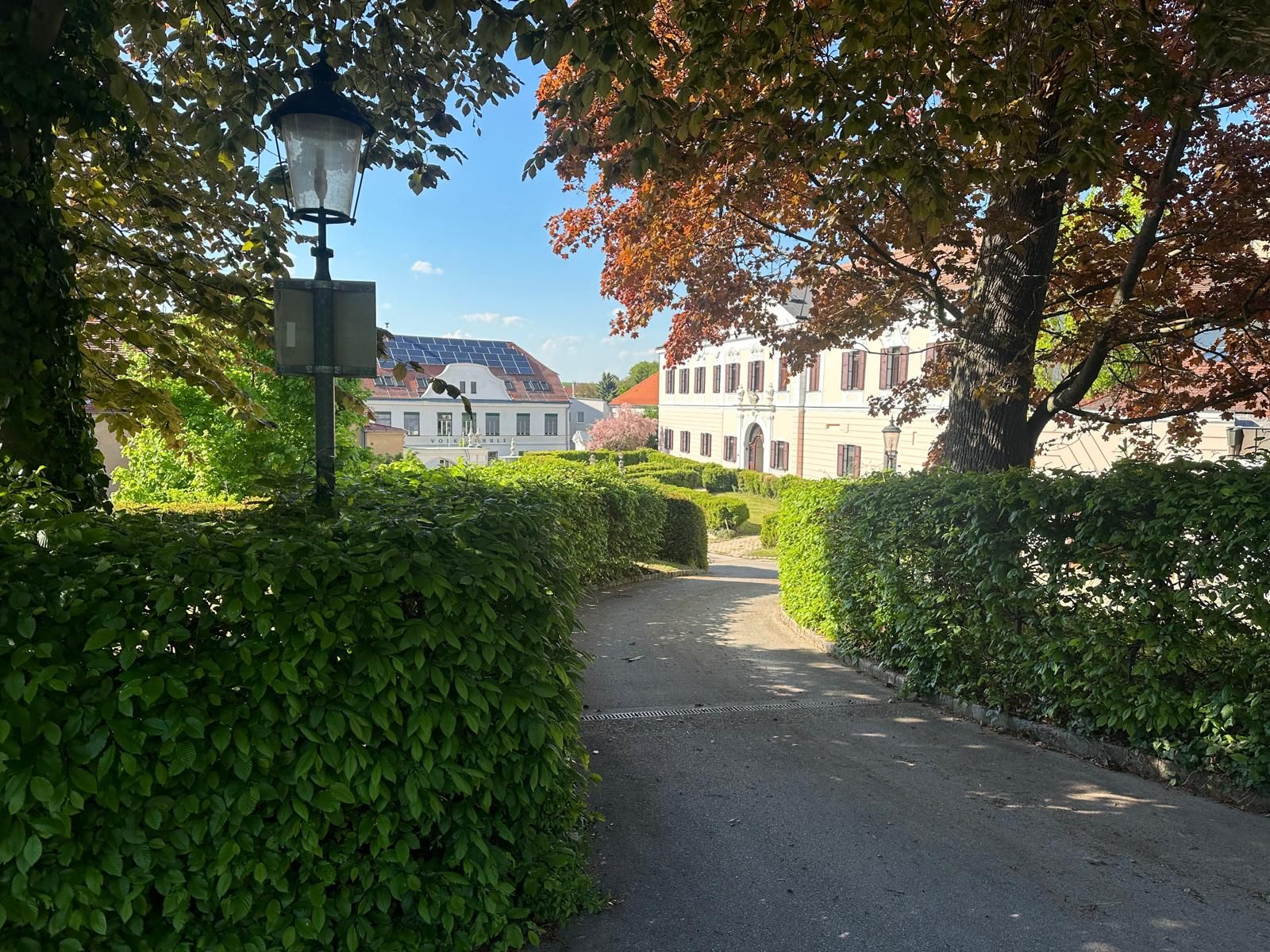 Pohľad na hrad v Großrußbachu, obklopený stromami a živým plotom, s lampášom v popredí.