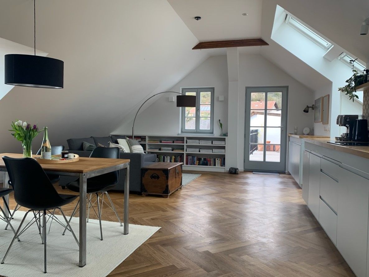 Moderný podkrovný byt s drevenou podlahou, jedálenským stolom, pohovkou a prístupom na balkón.