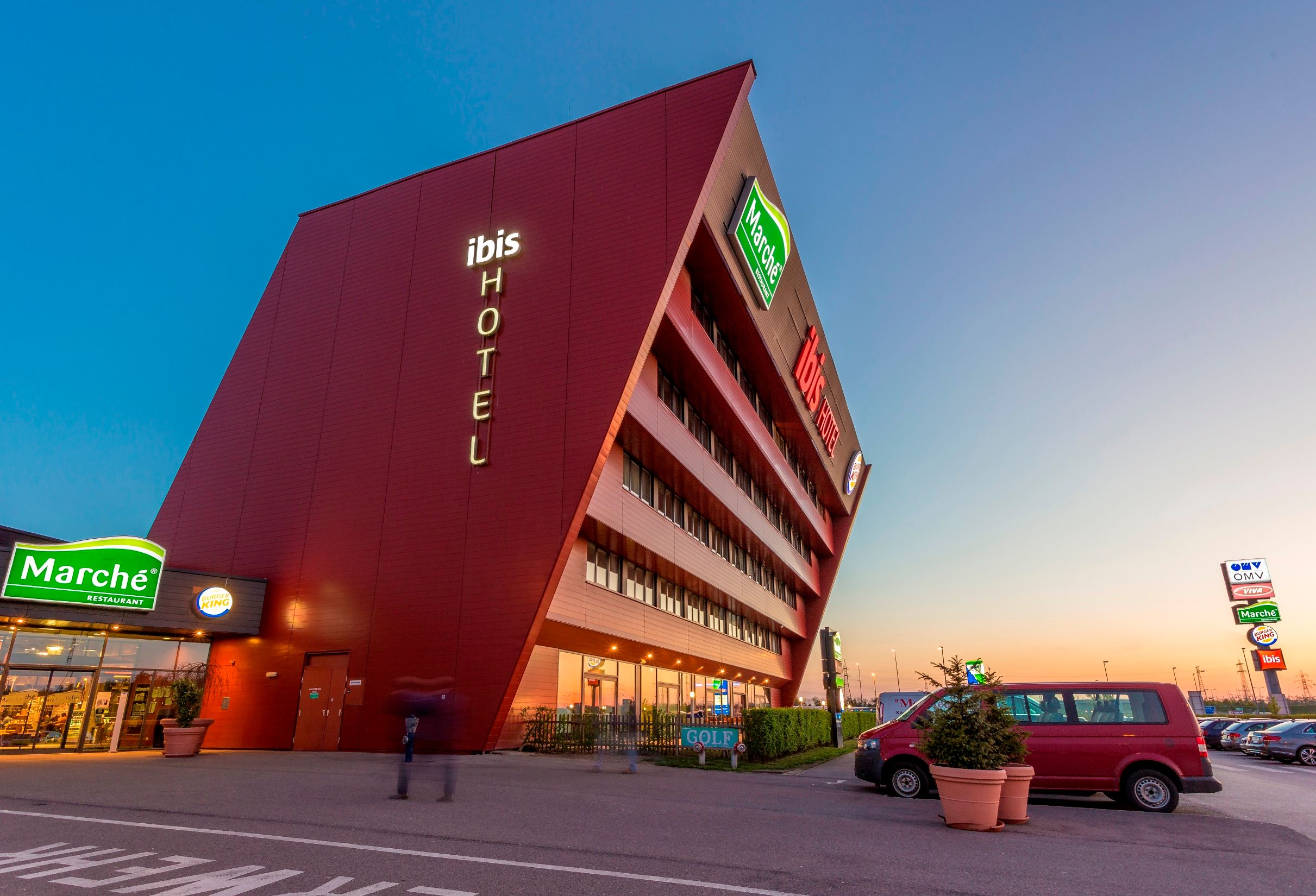 Moderná hotelová budova so šikmou fasádou a osvetleným nápisom "ibis HOTEL".