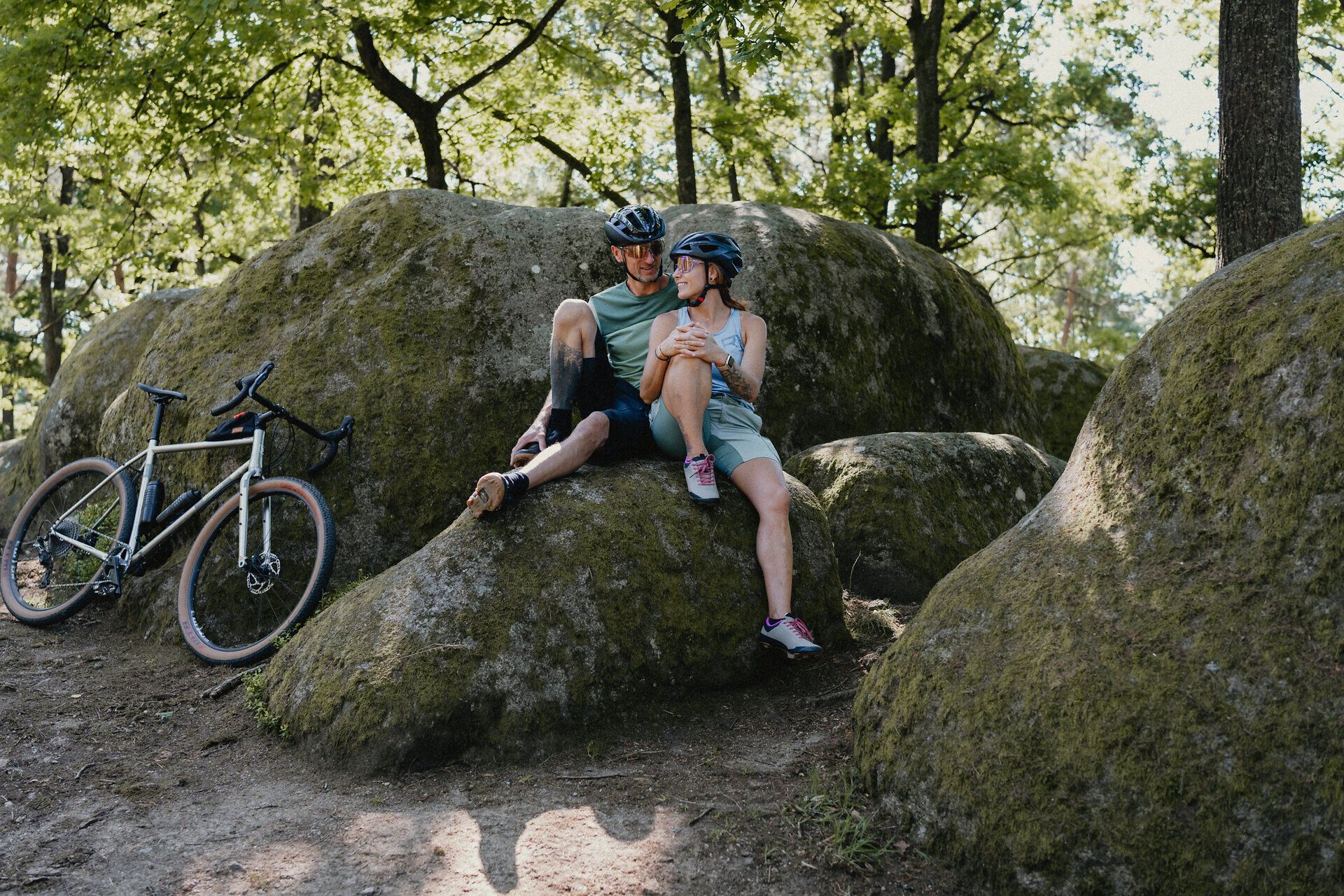 Muž a žena v cyklistickom oblečení sedia na kameni a rozprávajú sa, ich bicykle sú opreté o ďalší kameň vedľa nich.