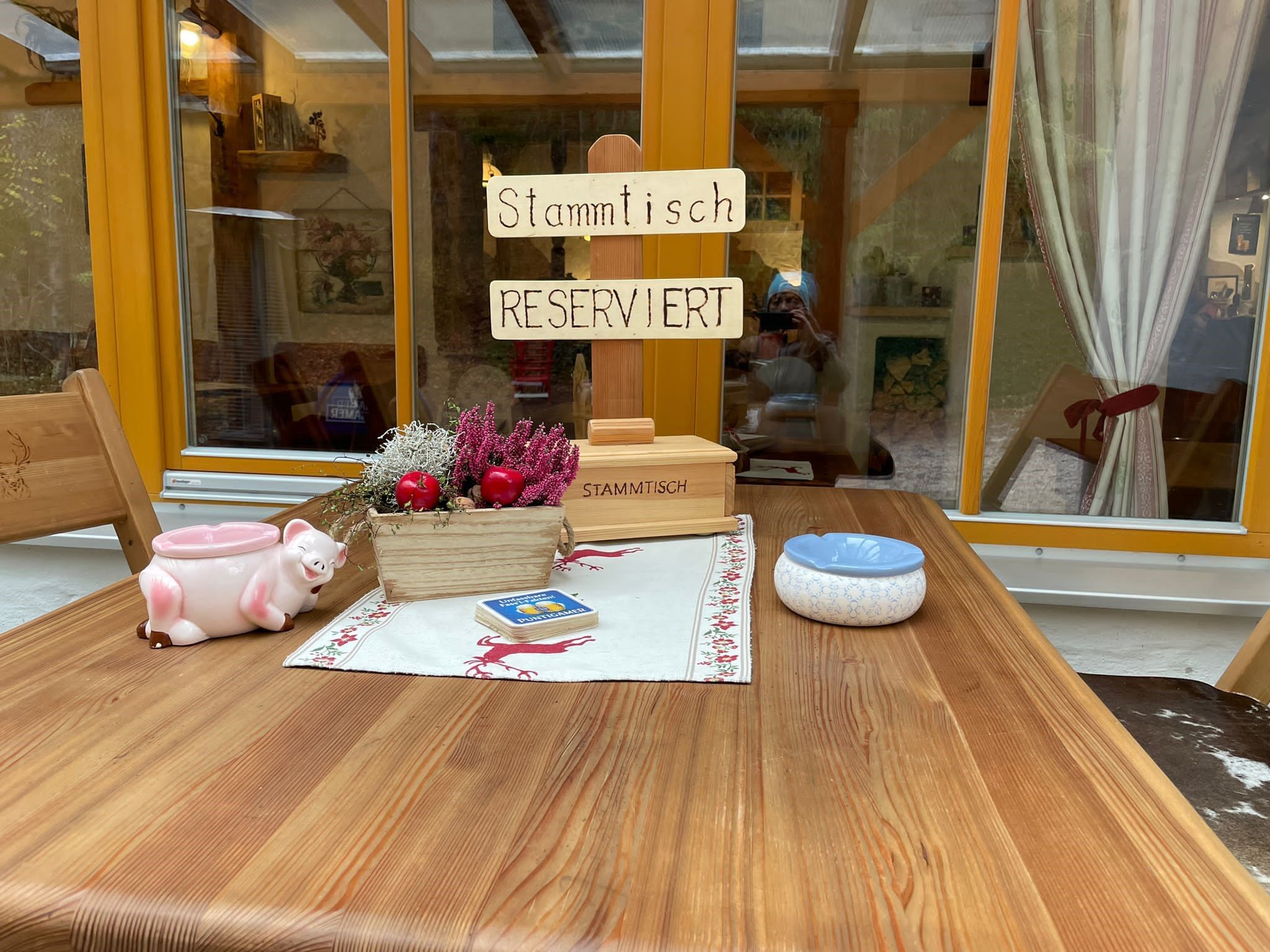 Rustikálny stôl s nápisom "Stammtisch Reserviert", dekoráciami a popolníkom.
