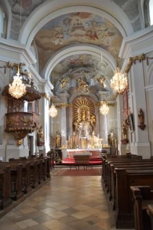 Pohľad do interiéru barokového kostola s oltárom, kazateľnicou a lustrami.
