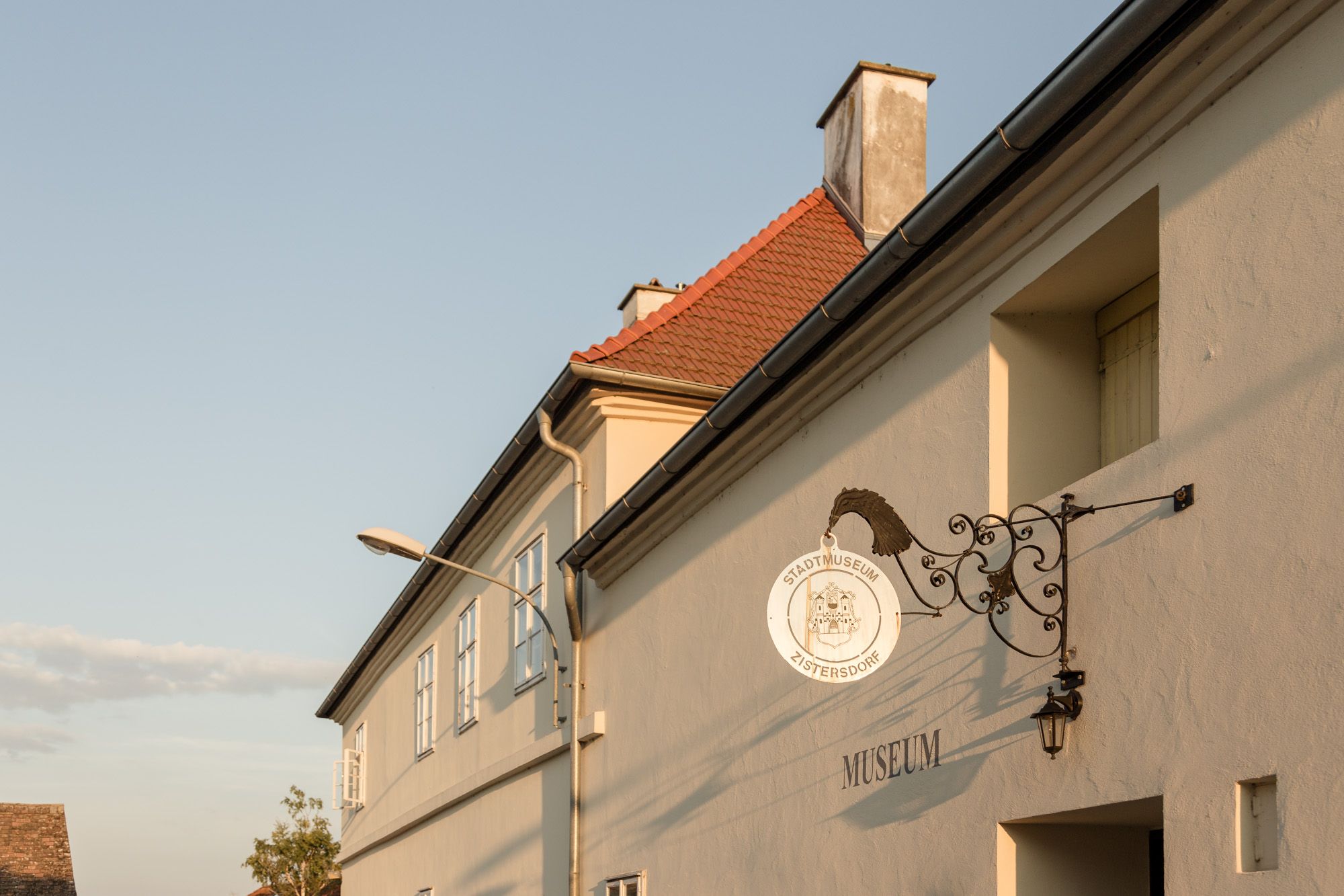 Exteriérový pohľad na mestské múzeum v Zistersdorfe s ozdobným nápisom a stĺpom verejného osvetlenia v popredí.