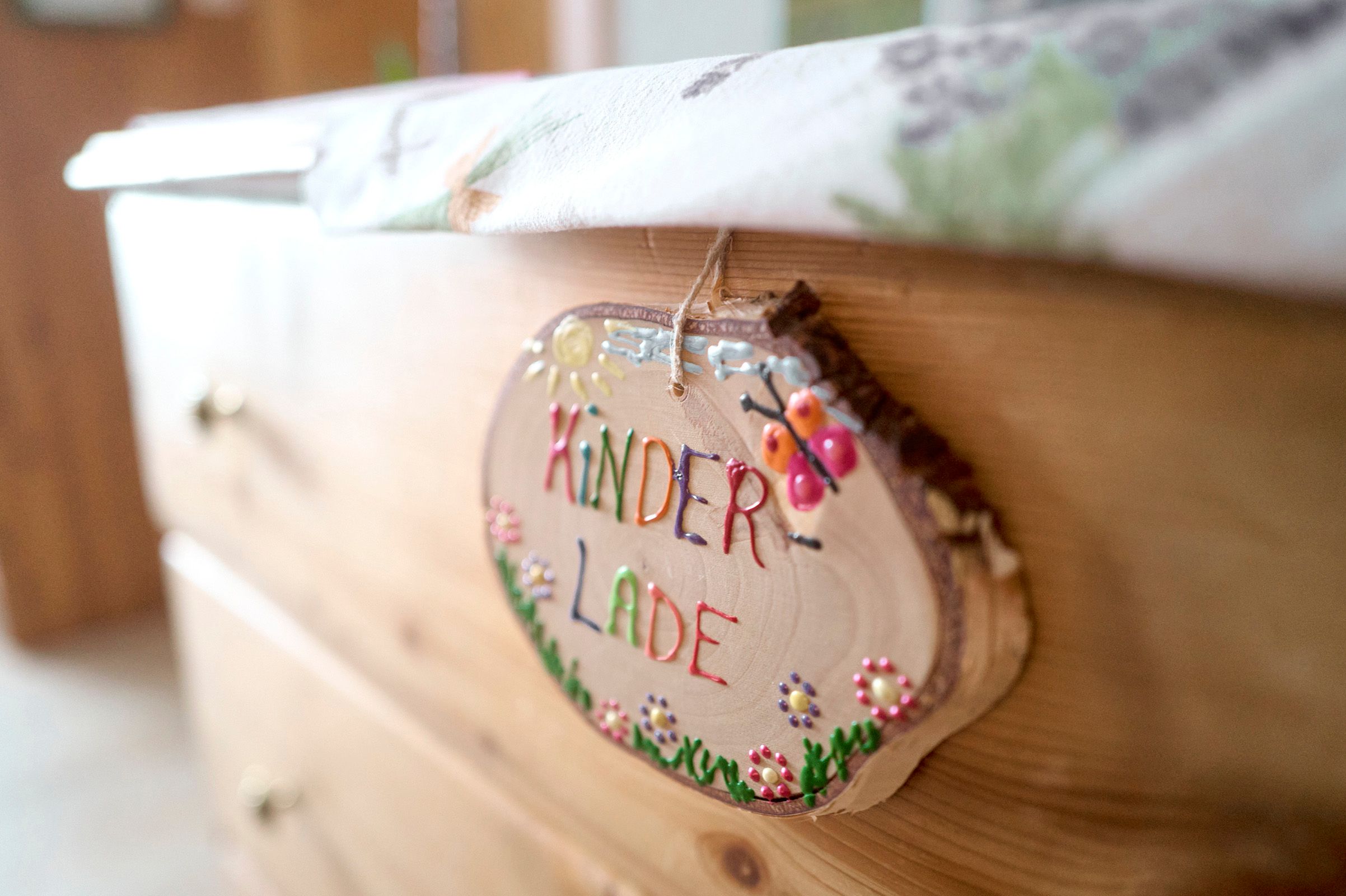 Detailný záber na drevenú tabuľu s nápisom "Kinderlade" na komode.