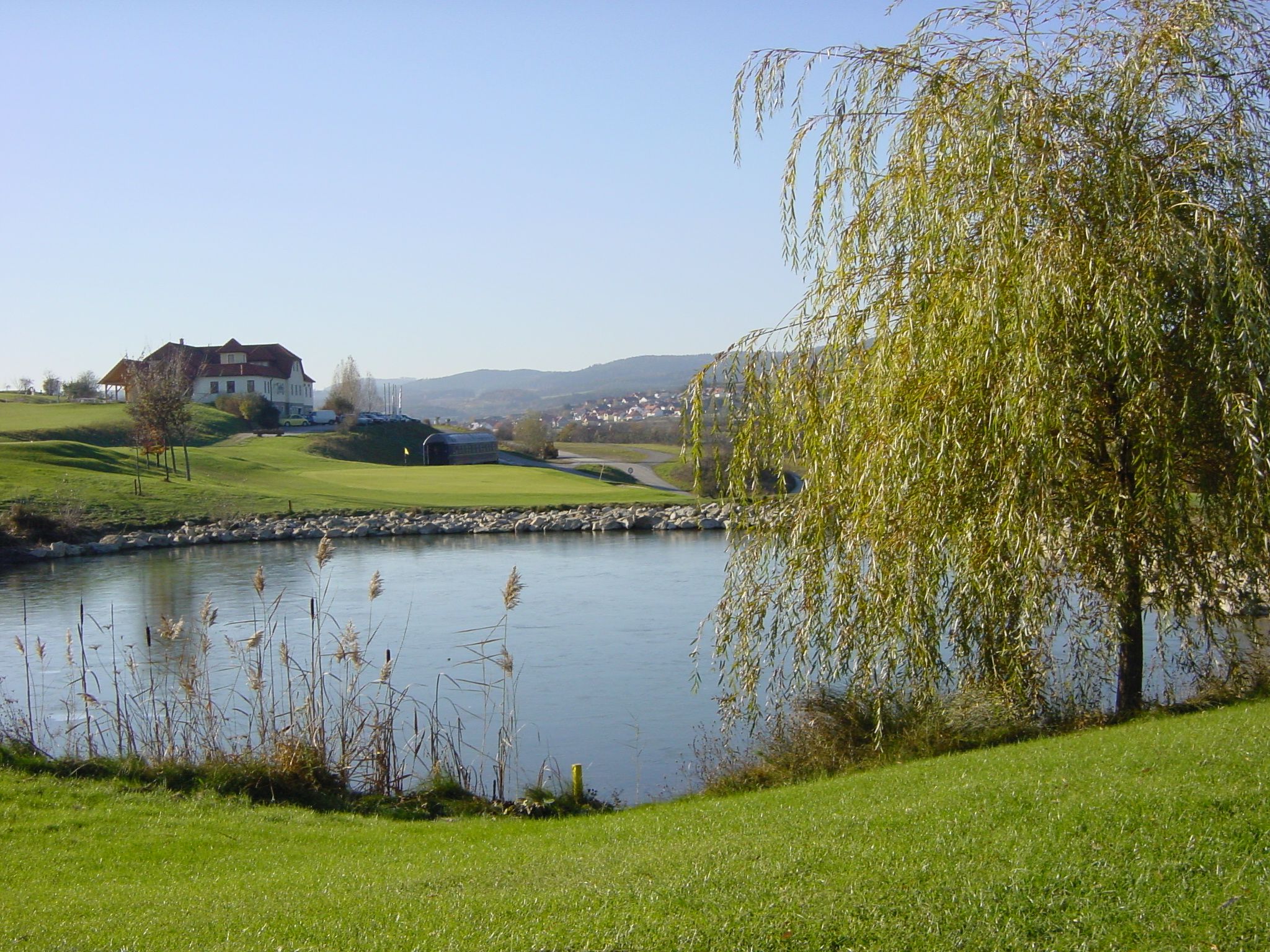 Krajina s golfovým ihriskom, rybníkom a budovami v pozadí.